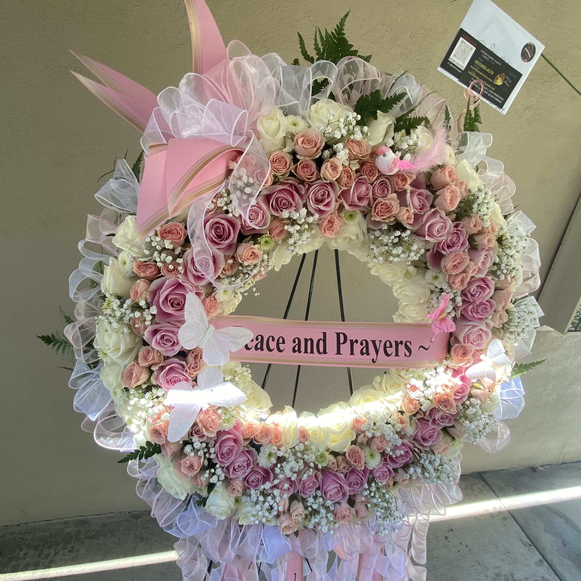 Large pink and white floral wreath on an easel with a "Peace and Prayers" ribbon.