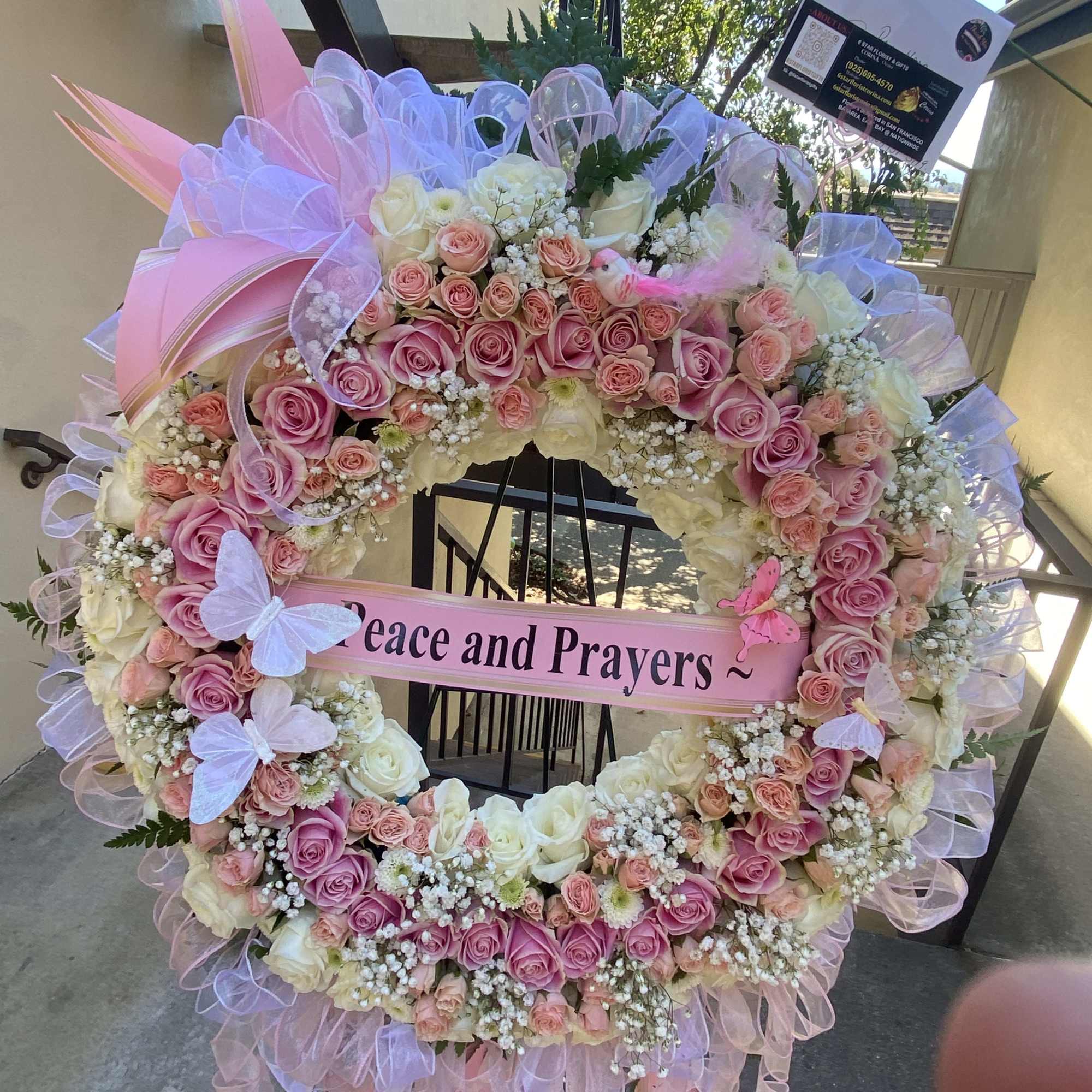 Large pink and white rose wreath with a "Peace and Prayers" ribbon