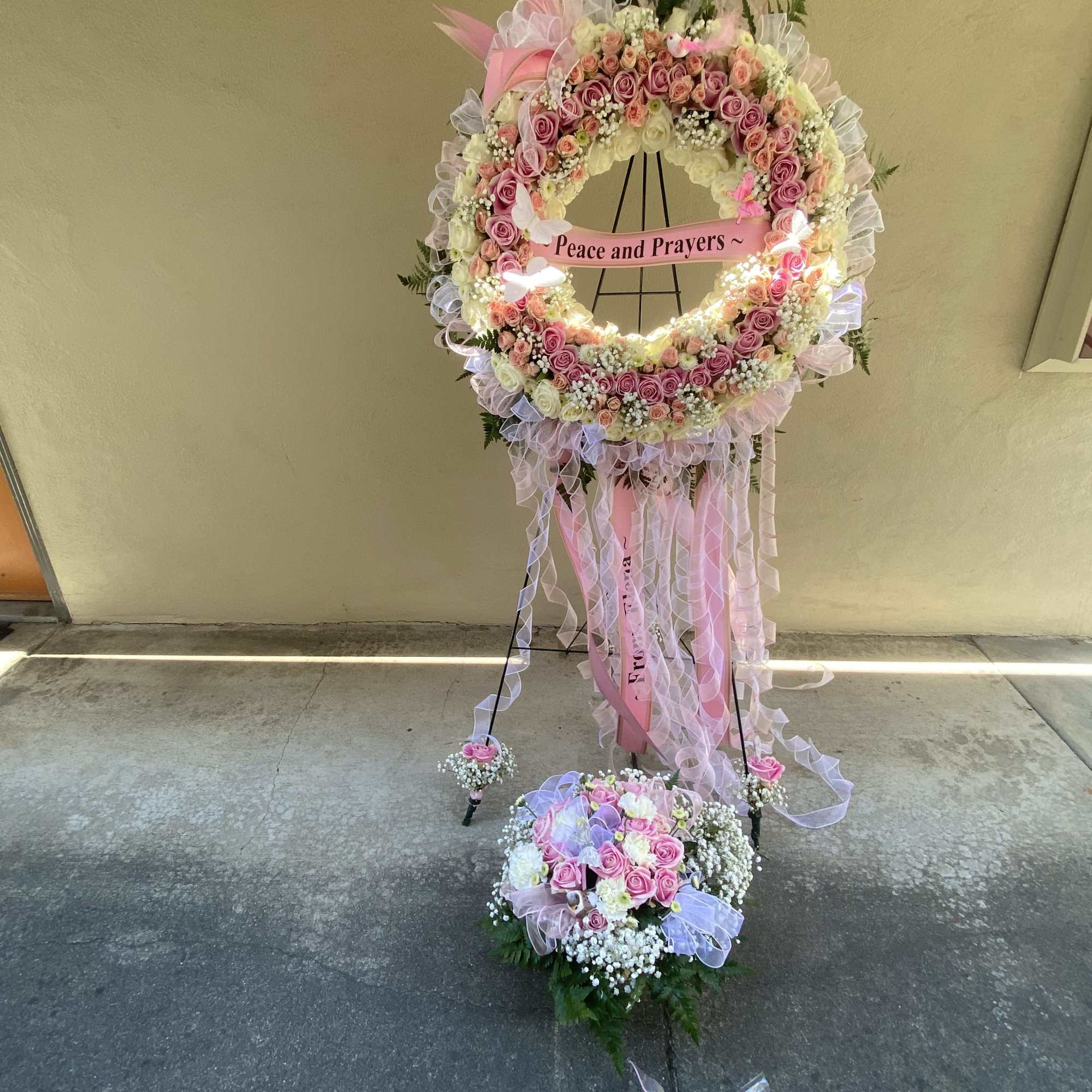 Pink and white floral standing wreath with a "Peace and Prayers" sign
