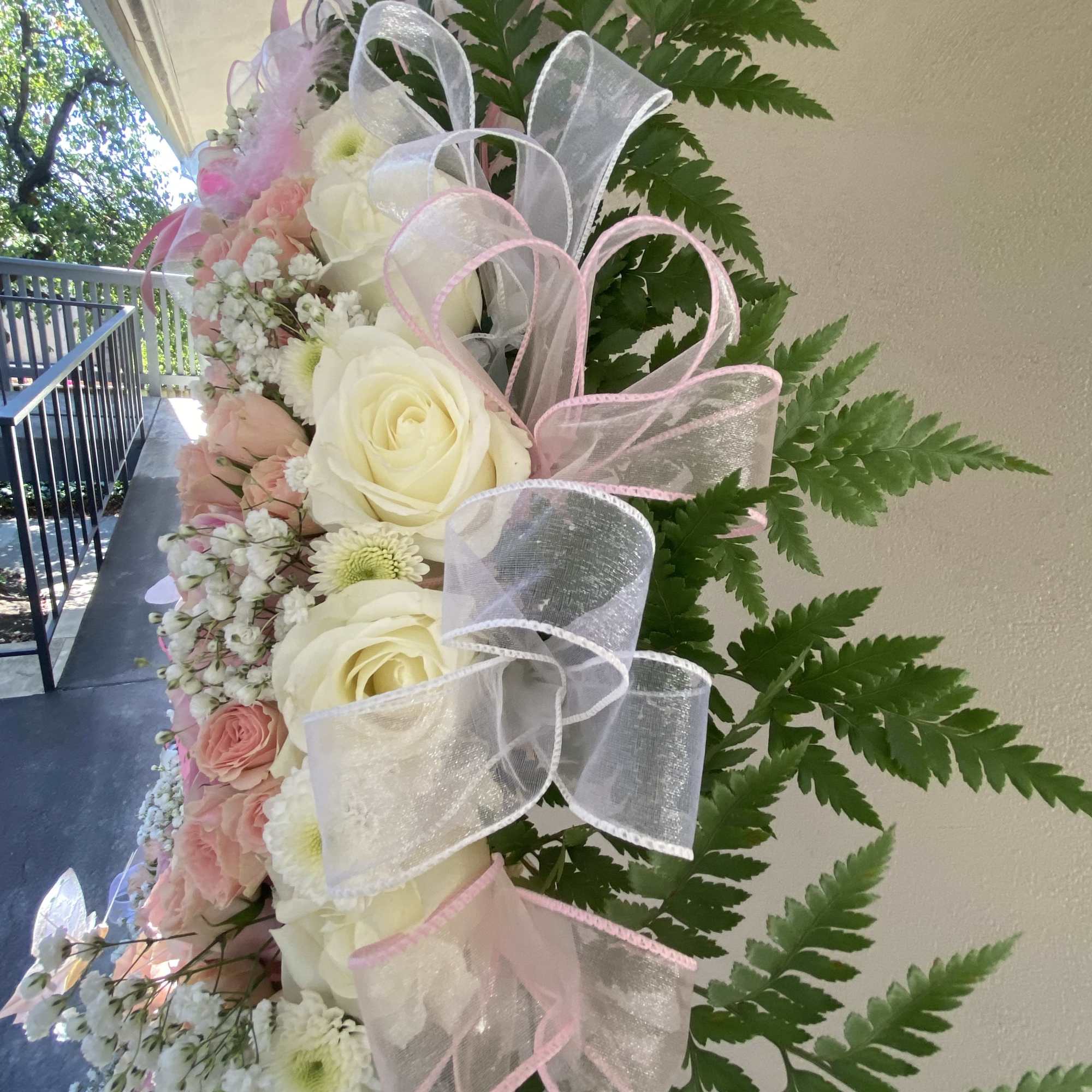 Pink and white floral spray with large ribbon bows and fern foliage