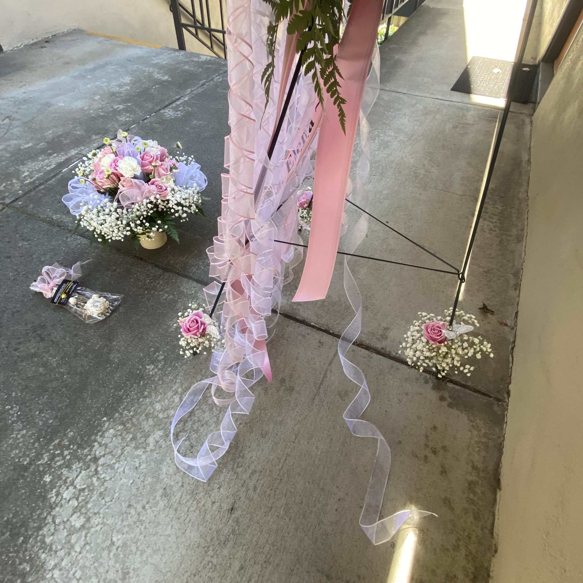 Pink rose arrangements with baby’s breath and ribbon on the ground near a stand