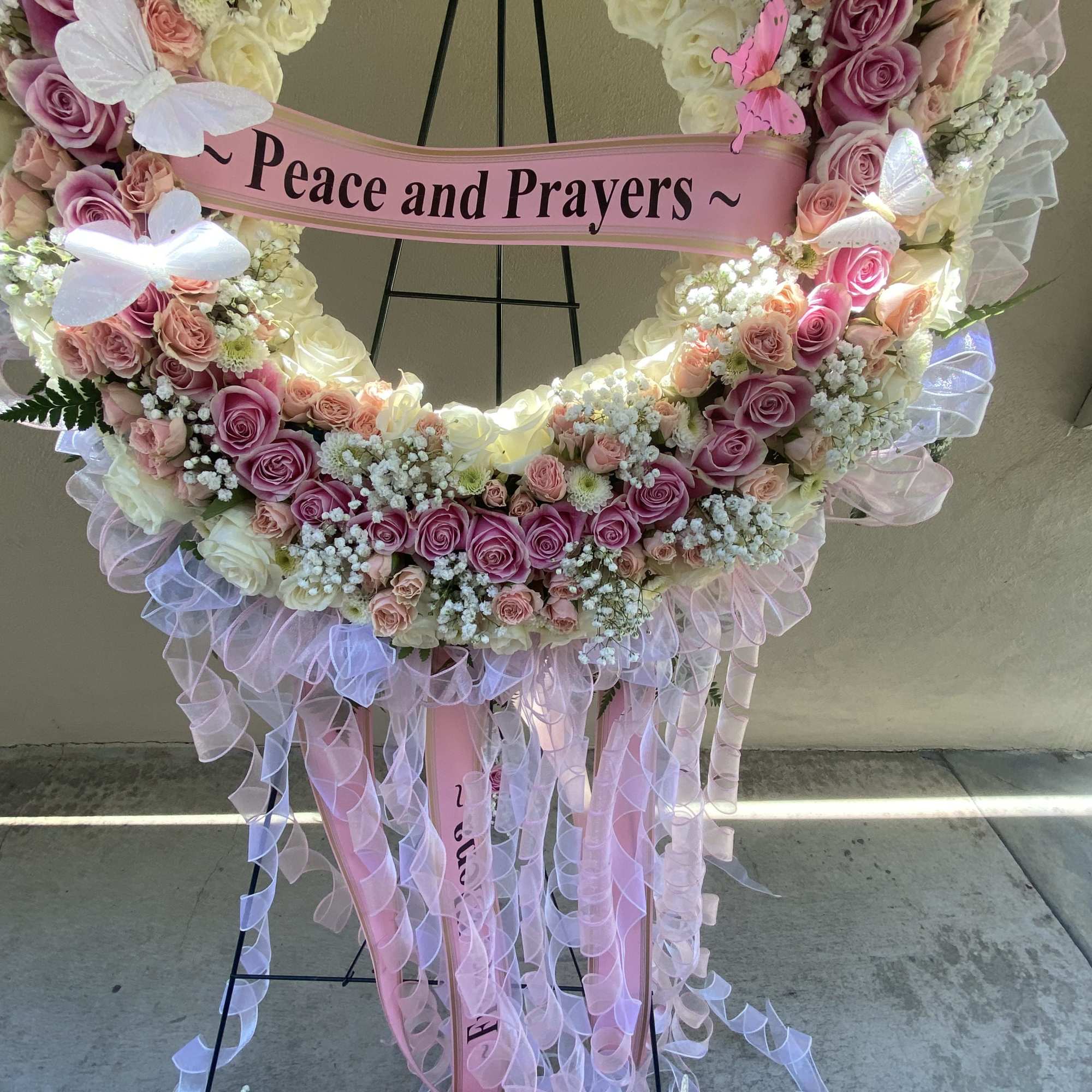 Pink and white rose funeral wreath with a "Peace and Prayers" ribbon