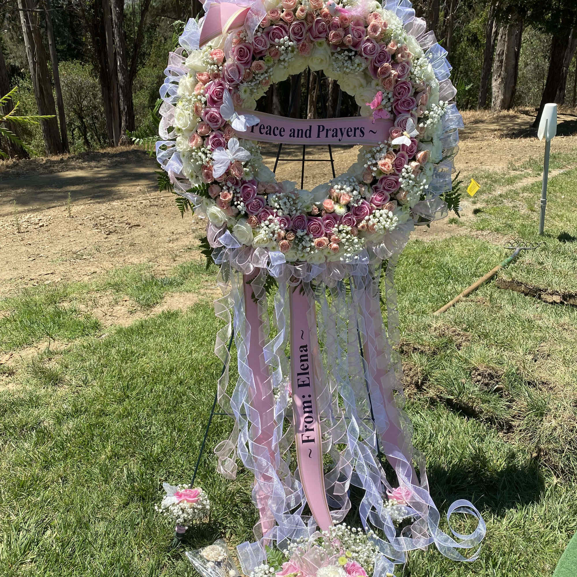 Large pink and white floral wreath with ribbons and a memorial sign