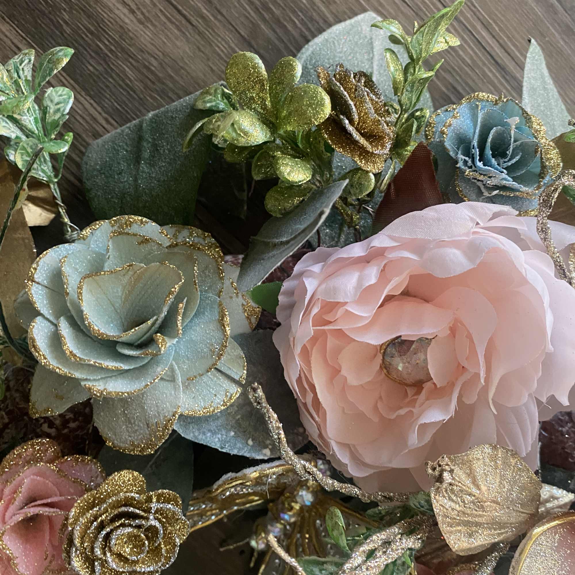 Artificial pastel flowers with gold glitter accents and green leaves