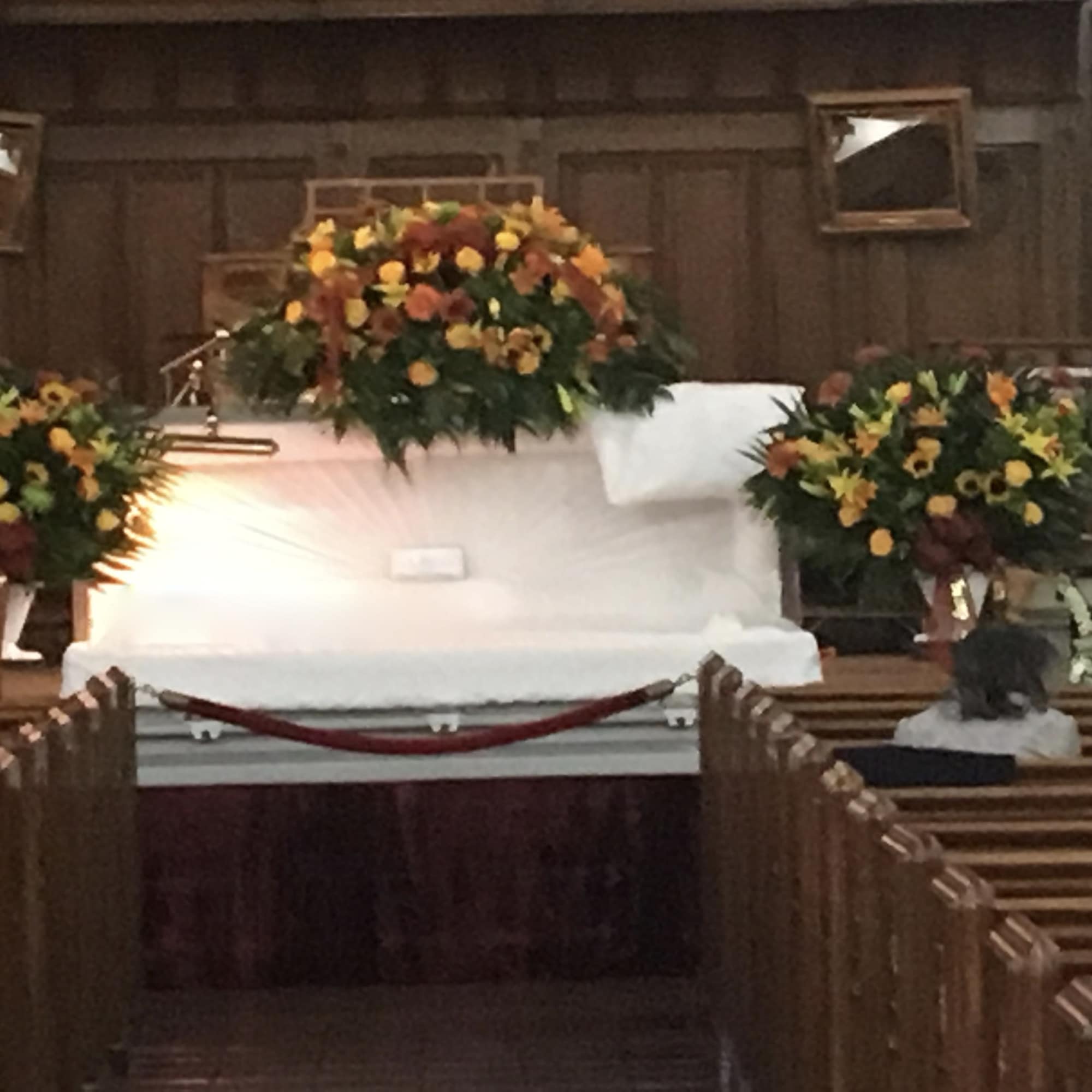 White casket surrounded by orange and yellow funeral flower sprays