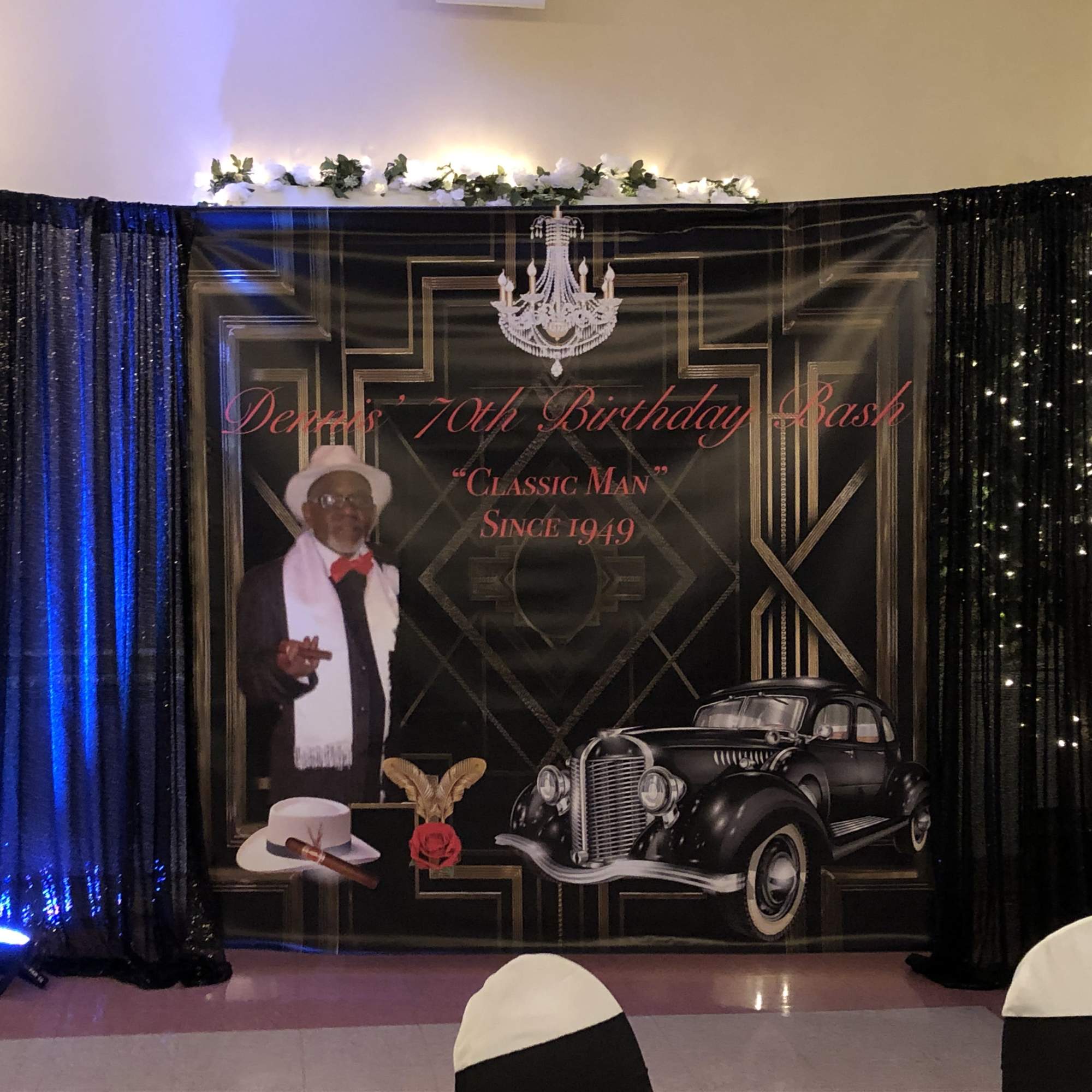 Birthday event backdrop with a man, vintage car graphic, and black drapes