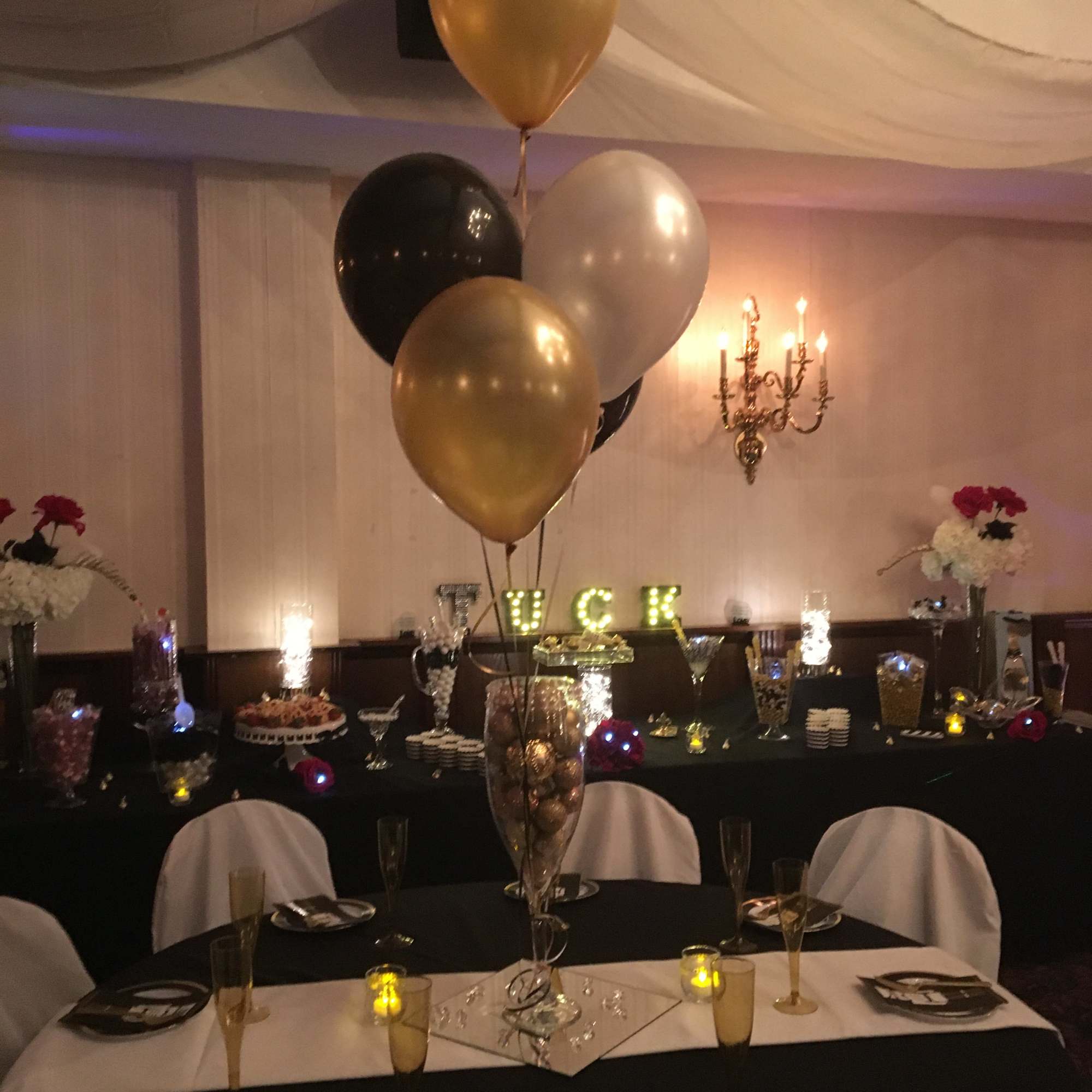 Balloon centerpiece at a decorated banquet table with gold, black, and white balloons