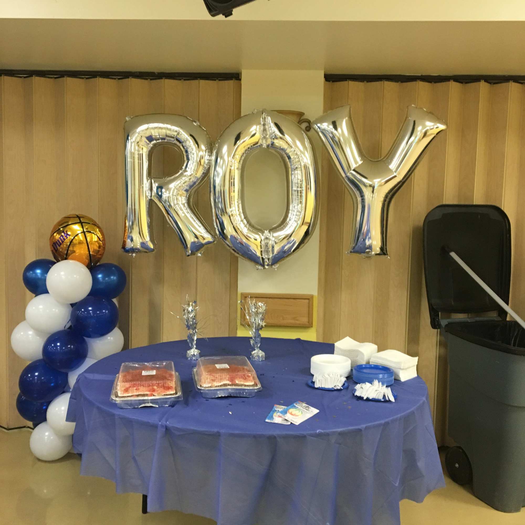 Silver "ROY" balloons above a blue table with snacks and balloon columns