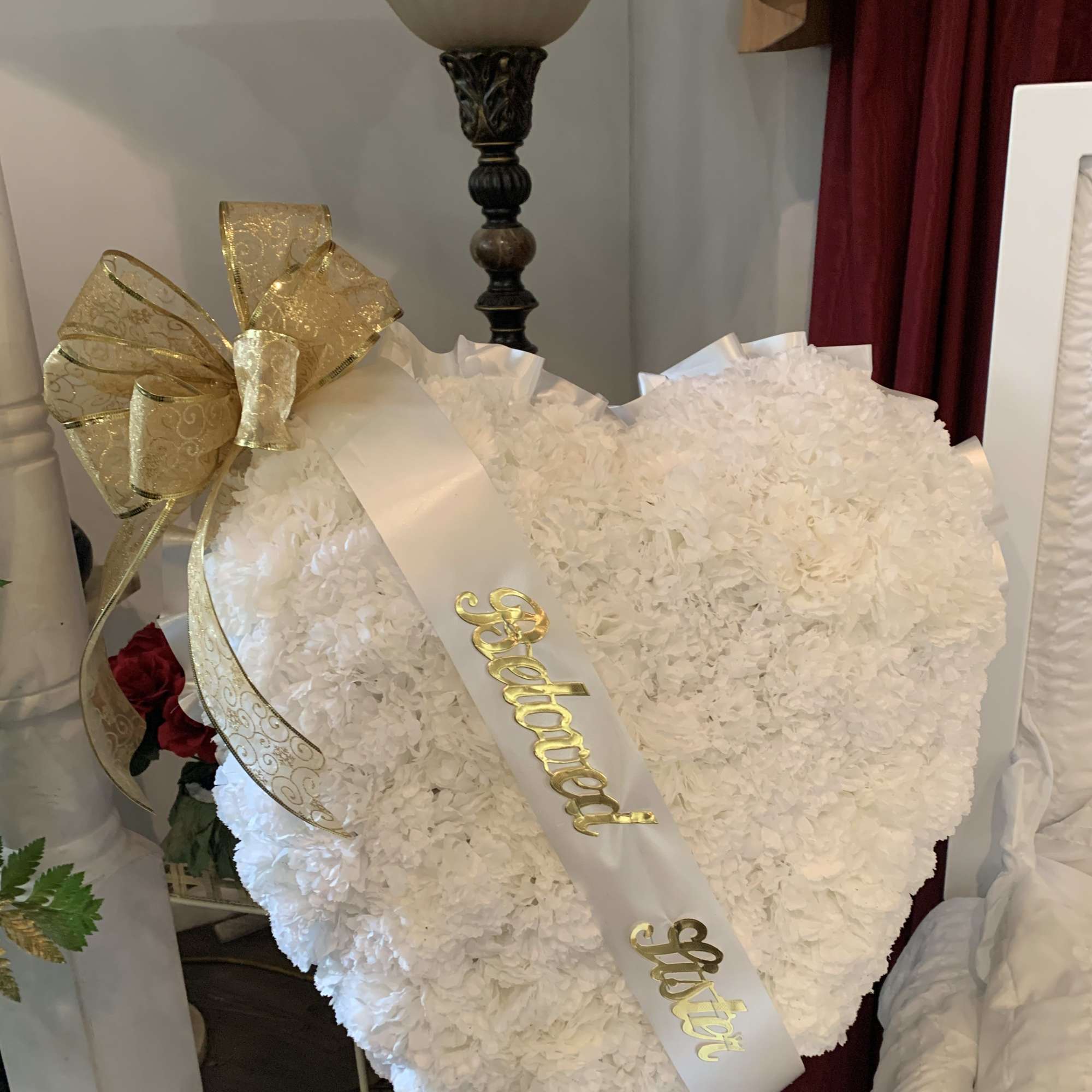 Heart-shaped white floral arrangement with a gold ribbon and sash