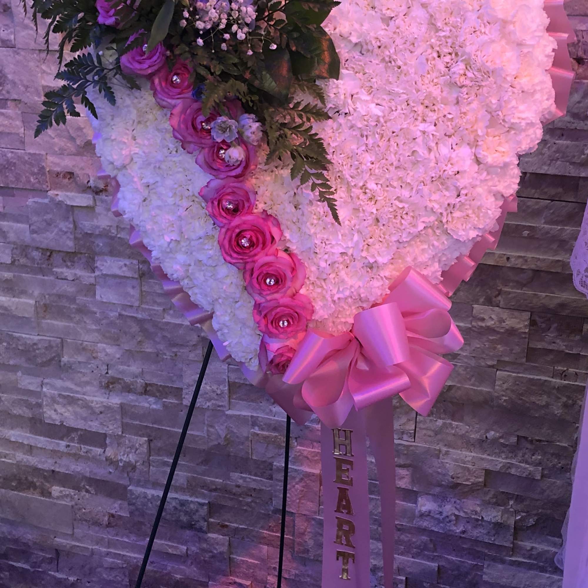 Heart-shaped floral stand with pink and white flowers and a ribbon
