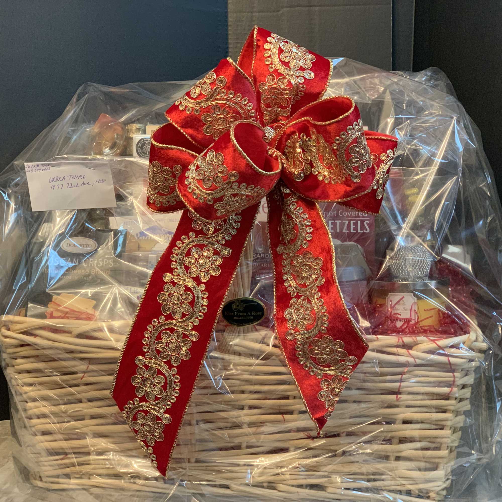 Gift basket wrapped in clear plastic with a large red decorative bow
