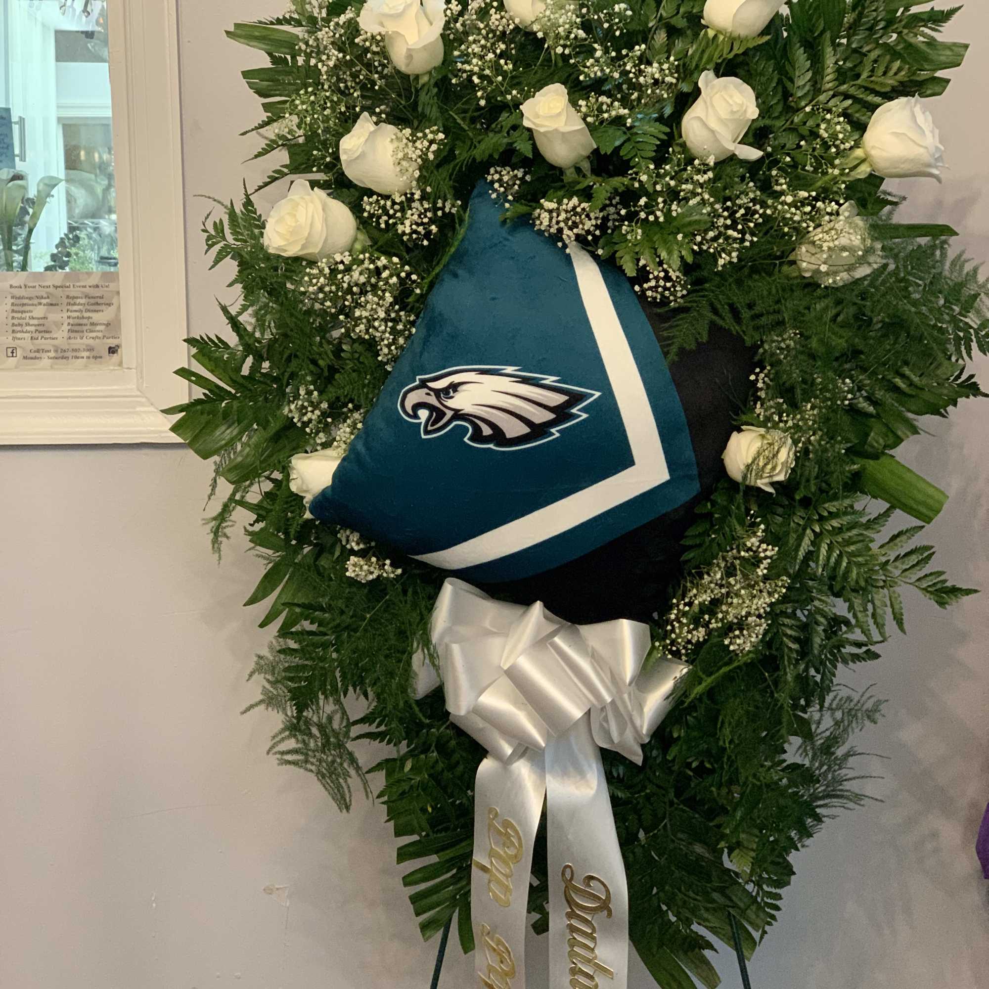 White rose funeral wreath with an Eagles jersey and ribbon