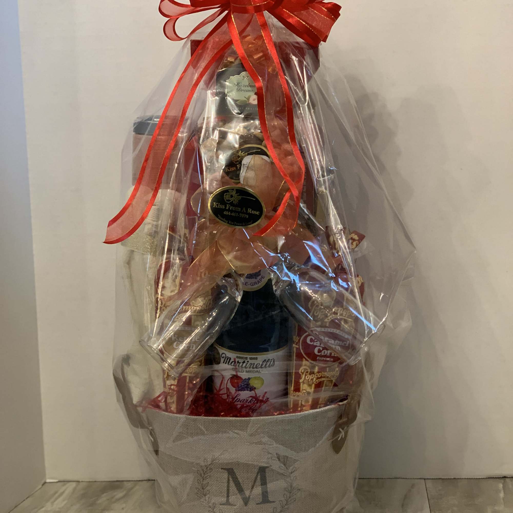 Gift basket with wine and snacks wrapped in clear cellophane and a red bow