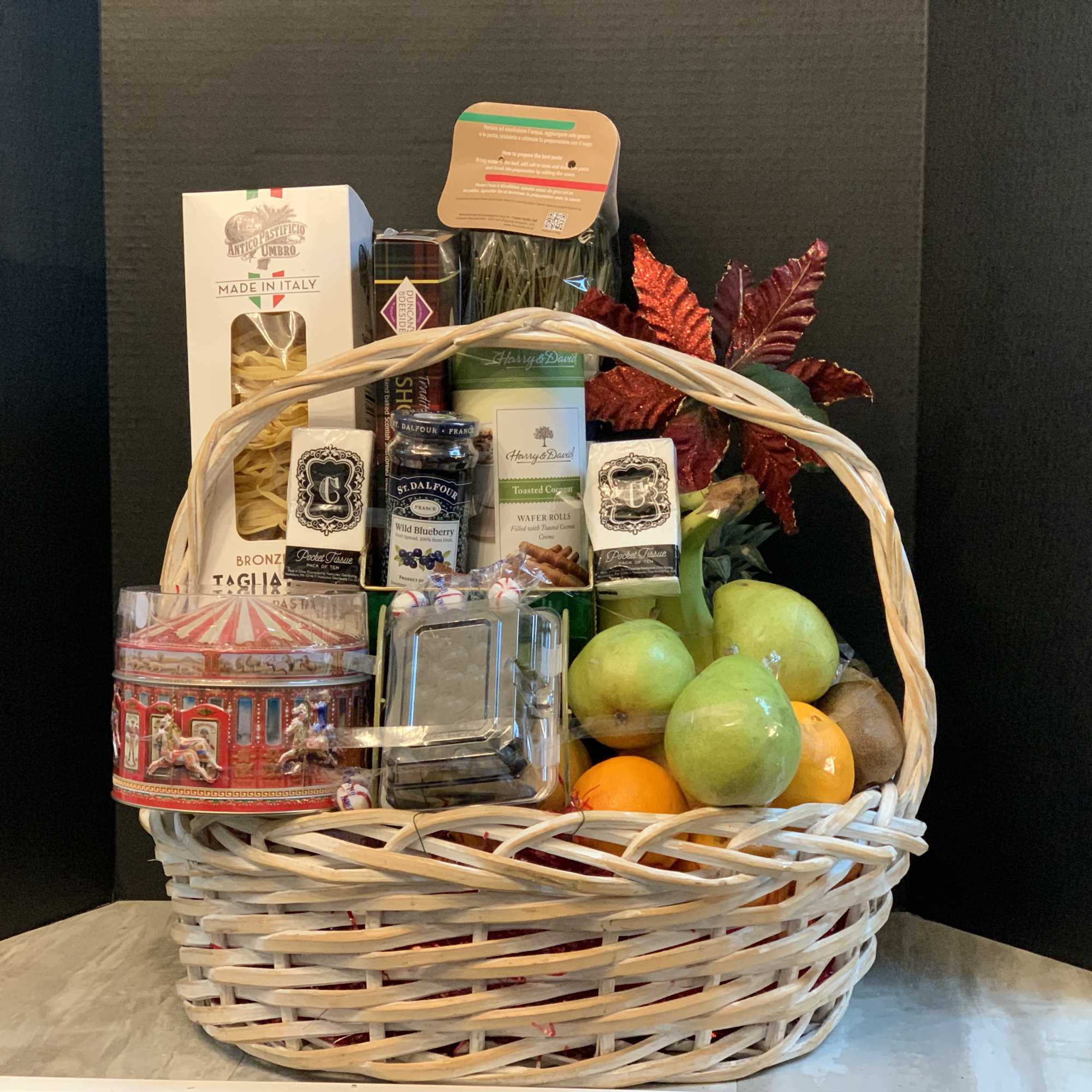 Gift basket with pasta, jam, cookies, fruit, and decorative leaves