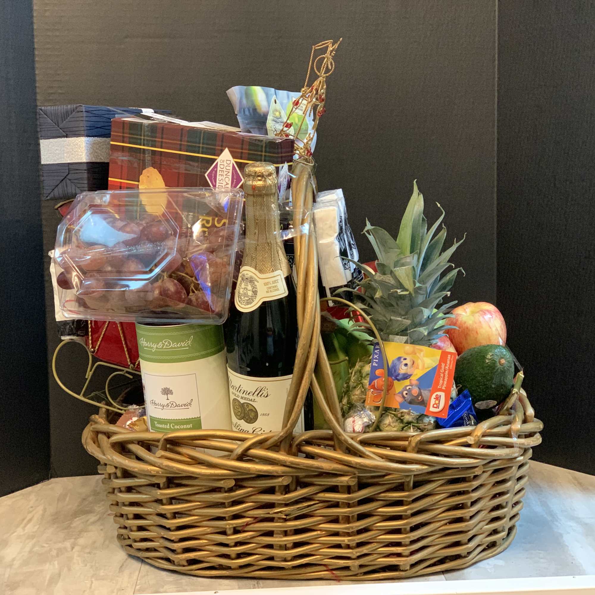 Gift basket with wine, chocolates, fruit, and snacks in a wicker tray
