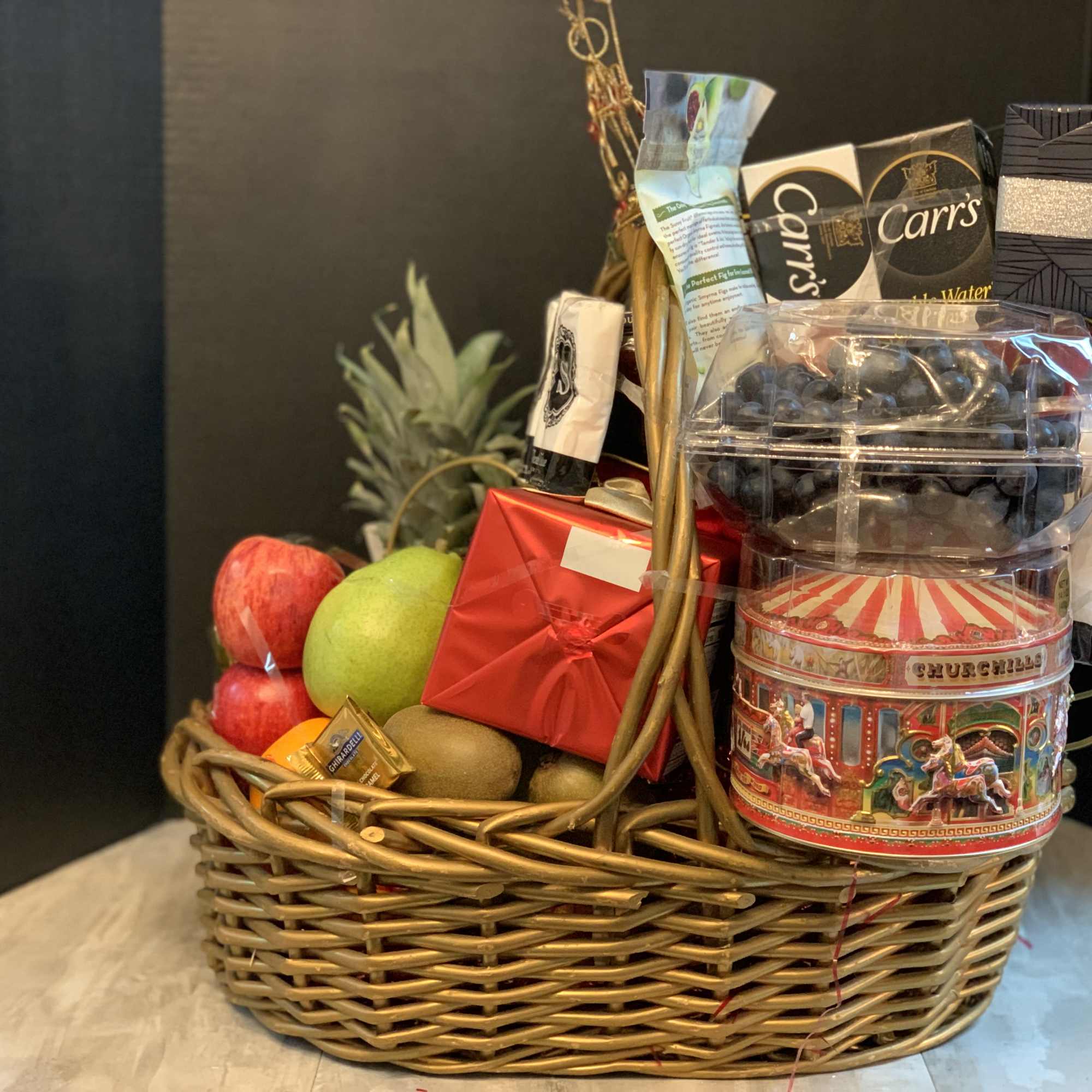 Gift basket with fruit, chocolates, and packaged snacks in a wicker basket