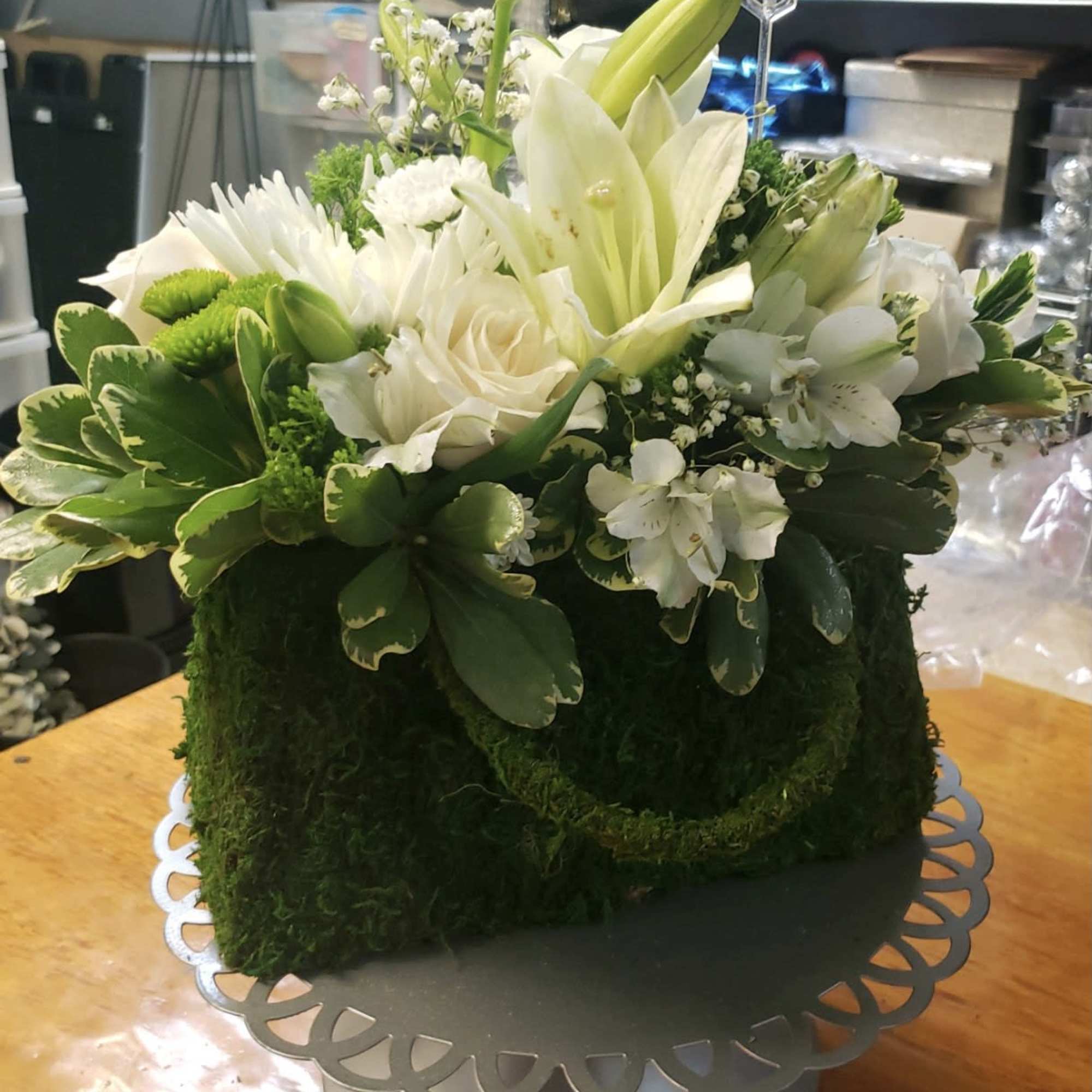 White floral arrangement in a moss-covered box on a silver stand
