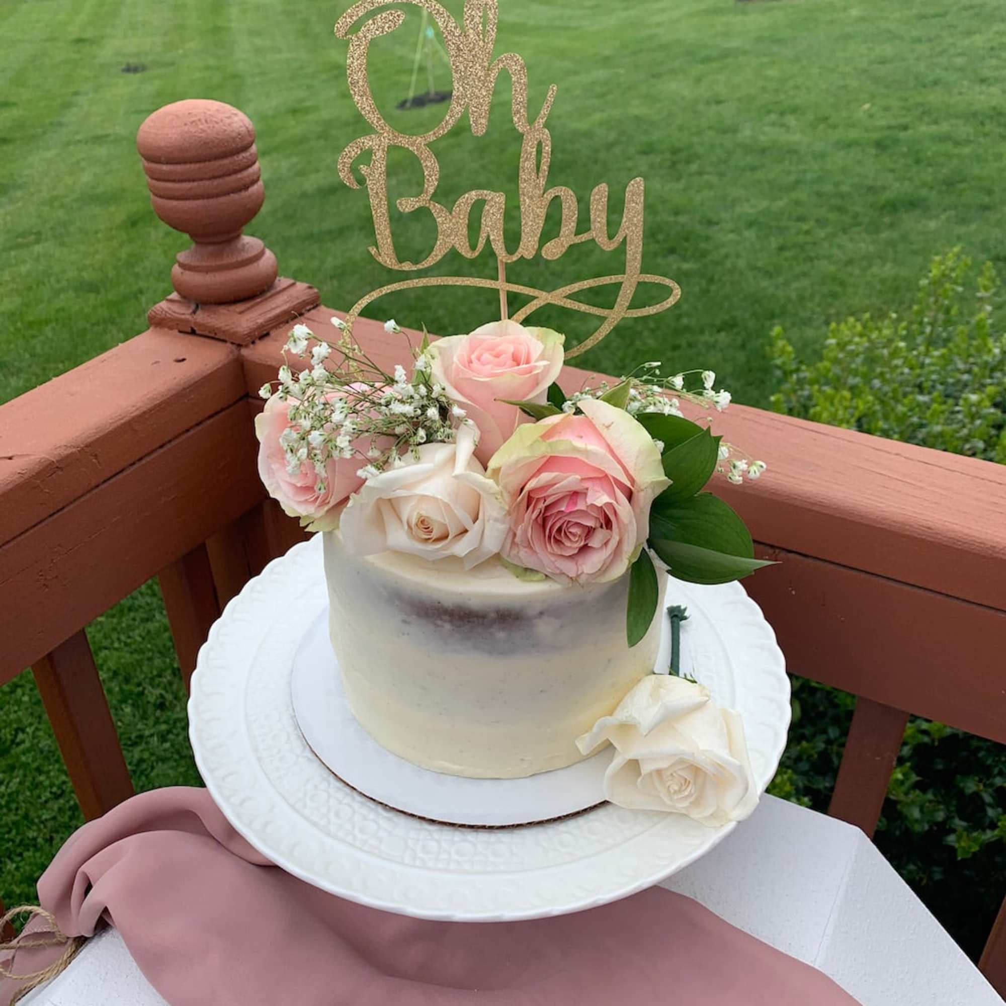 Small cake topped with pink and white roses and a glittery "Oh Baby" sign