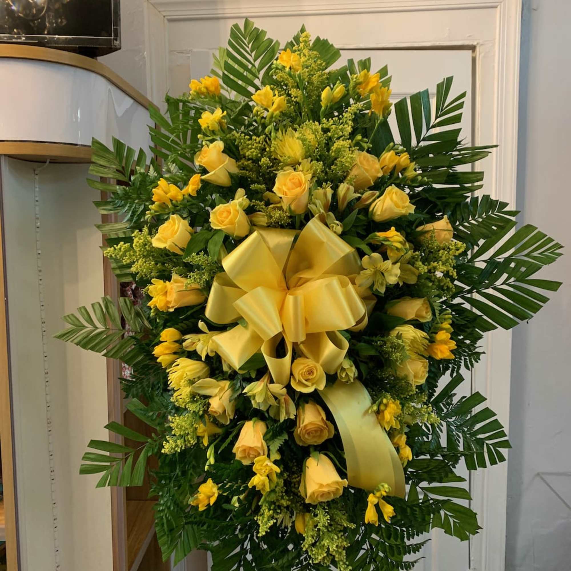 Yellow rose funeral spray with a large ribbon on a stand