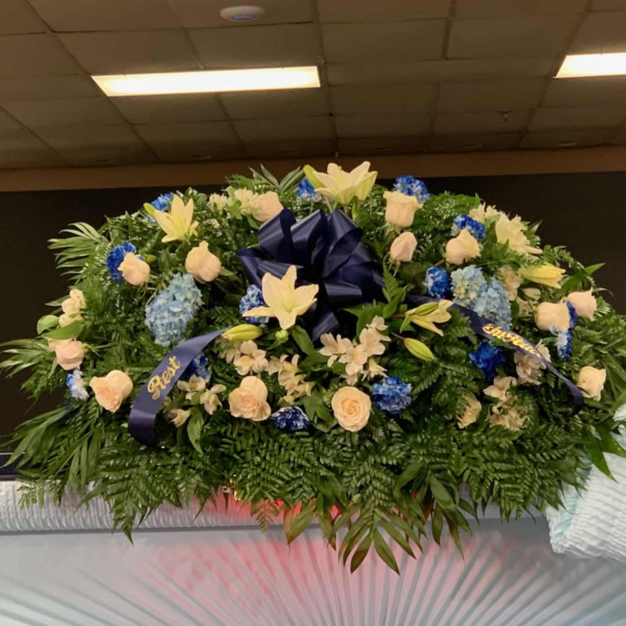 Large funeral spray with cream roses, lilies, and blue flowers