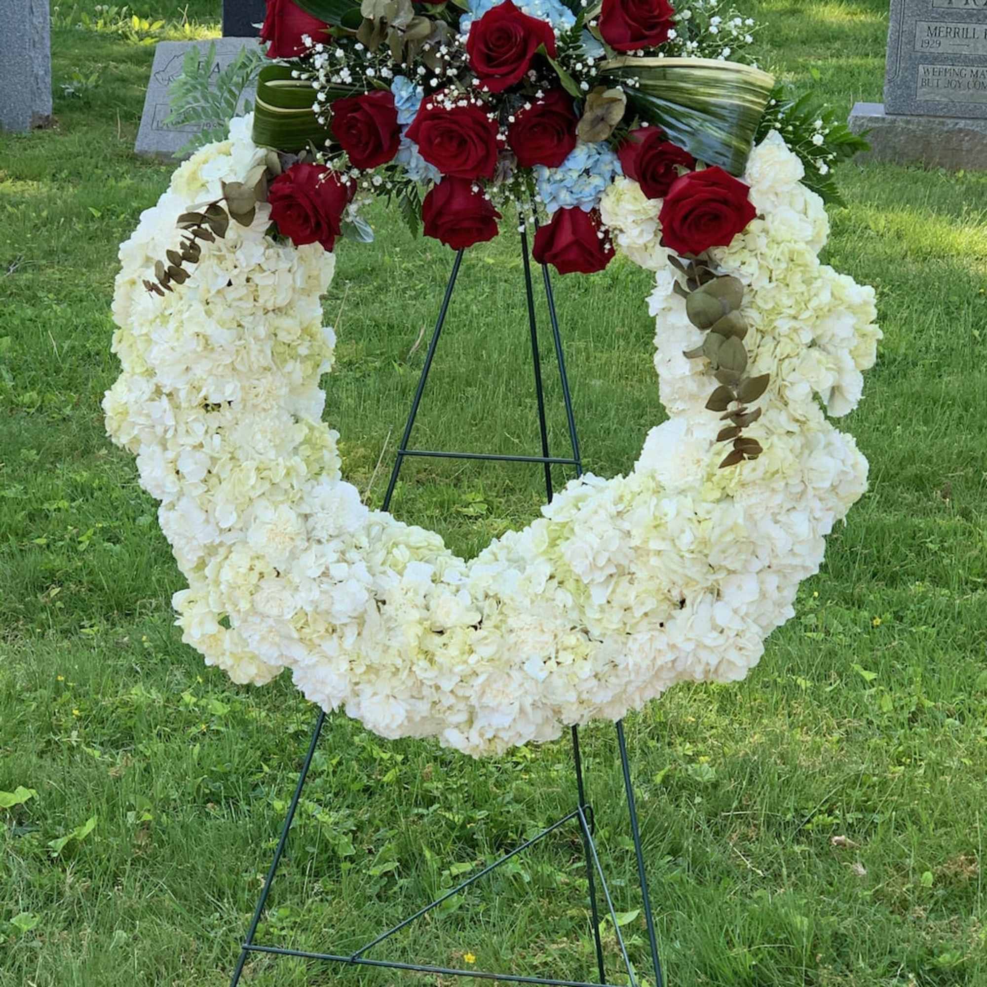 Standing funeral wreath with white flowers and red roses on an easel