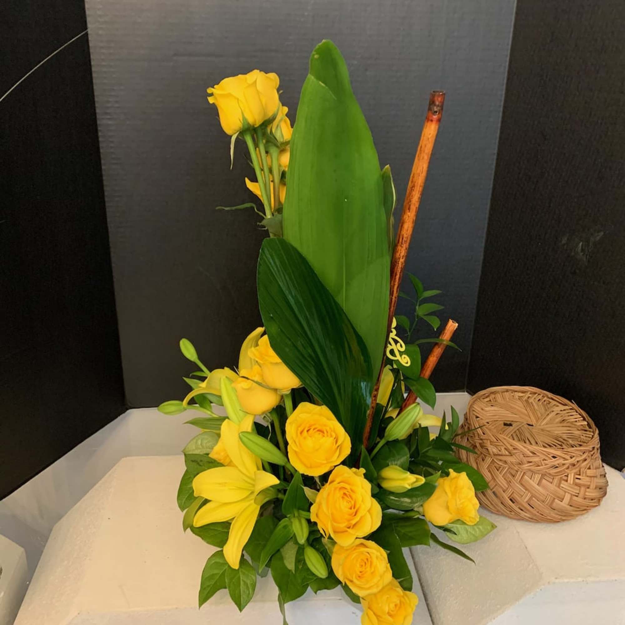 Yellow roses and lilies arranged with tall tropical leaves
