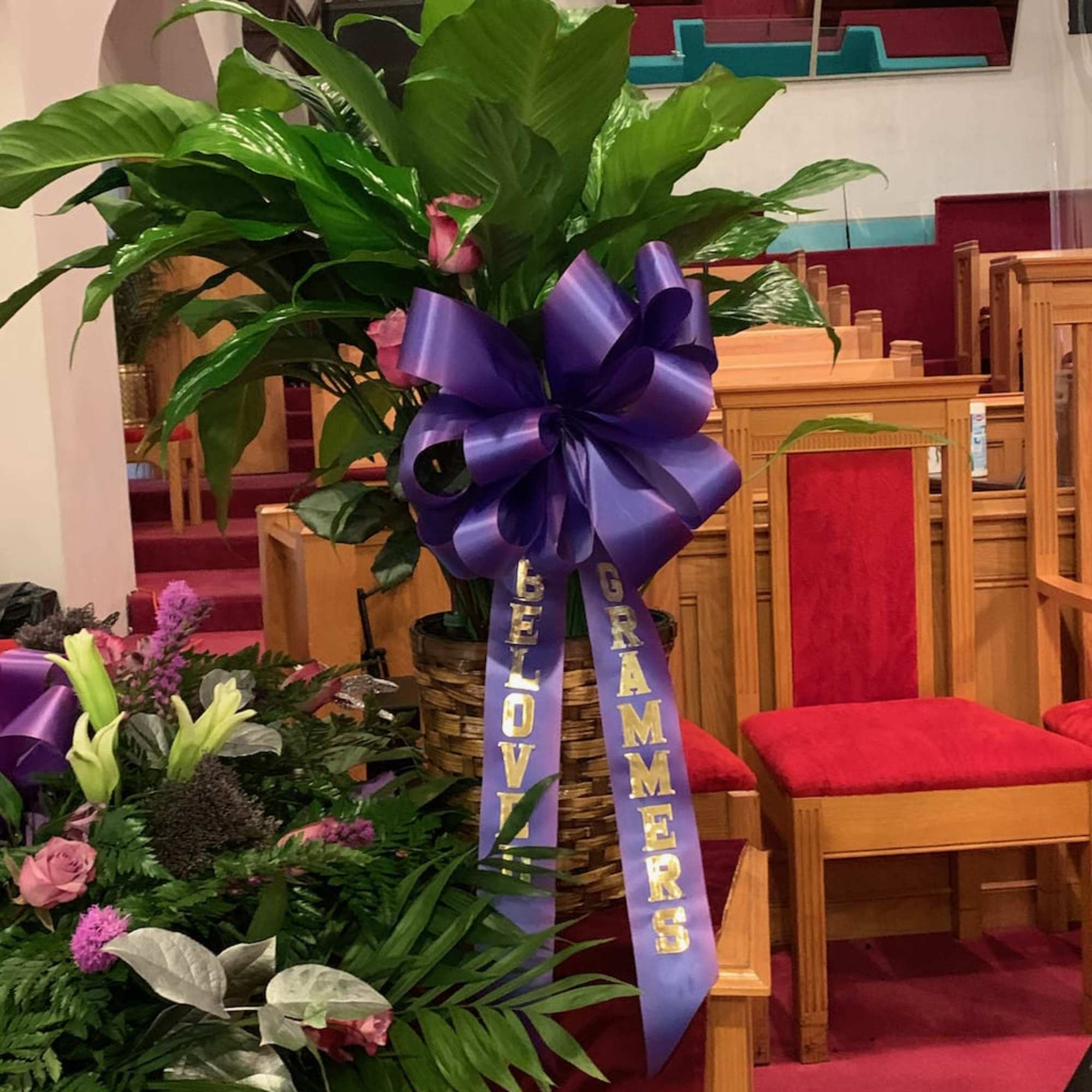 Large green plant arrangement with a purple ribbon in a church pew