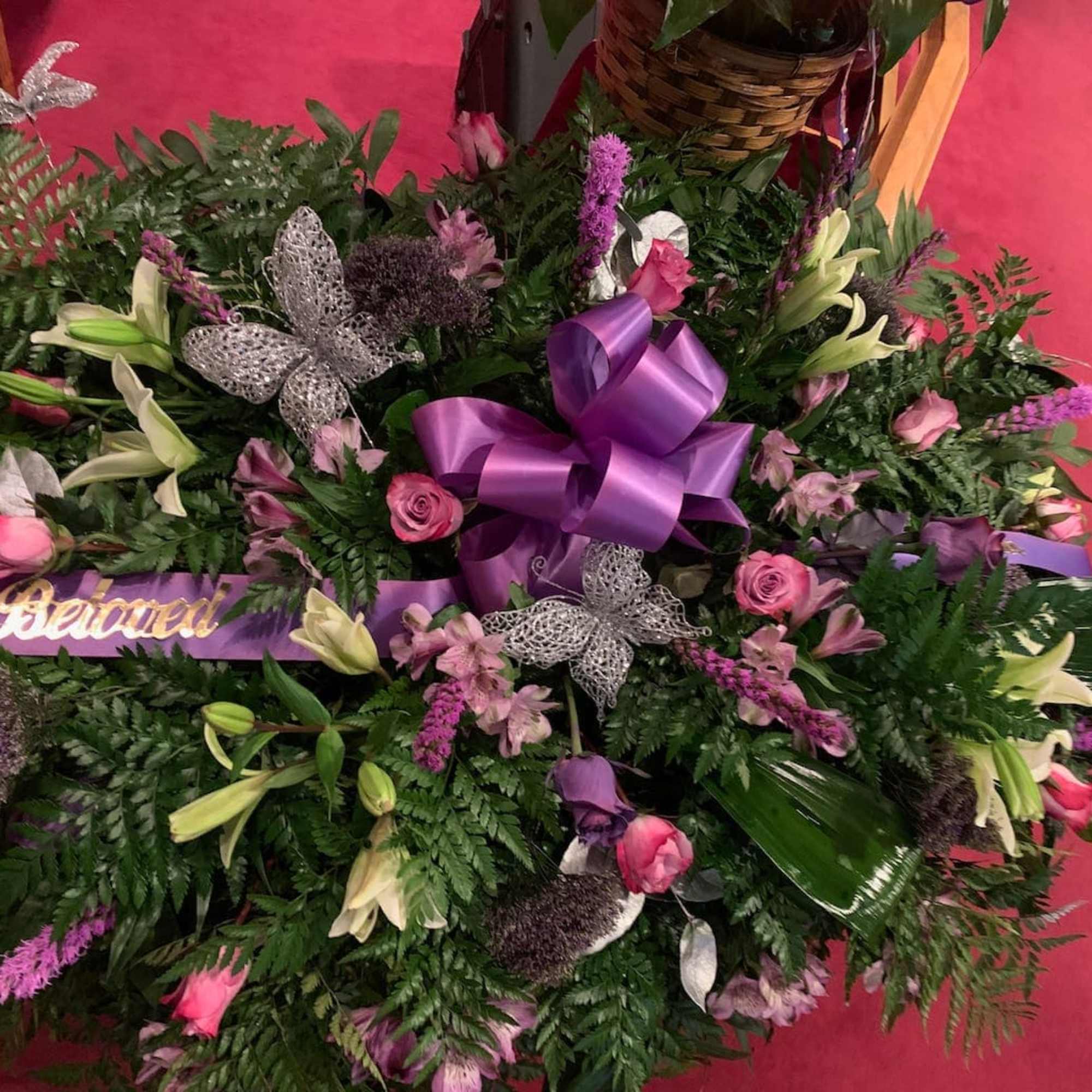 Large floral spray with pink roses, lilies, and purple ribbon on a pink floor