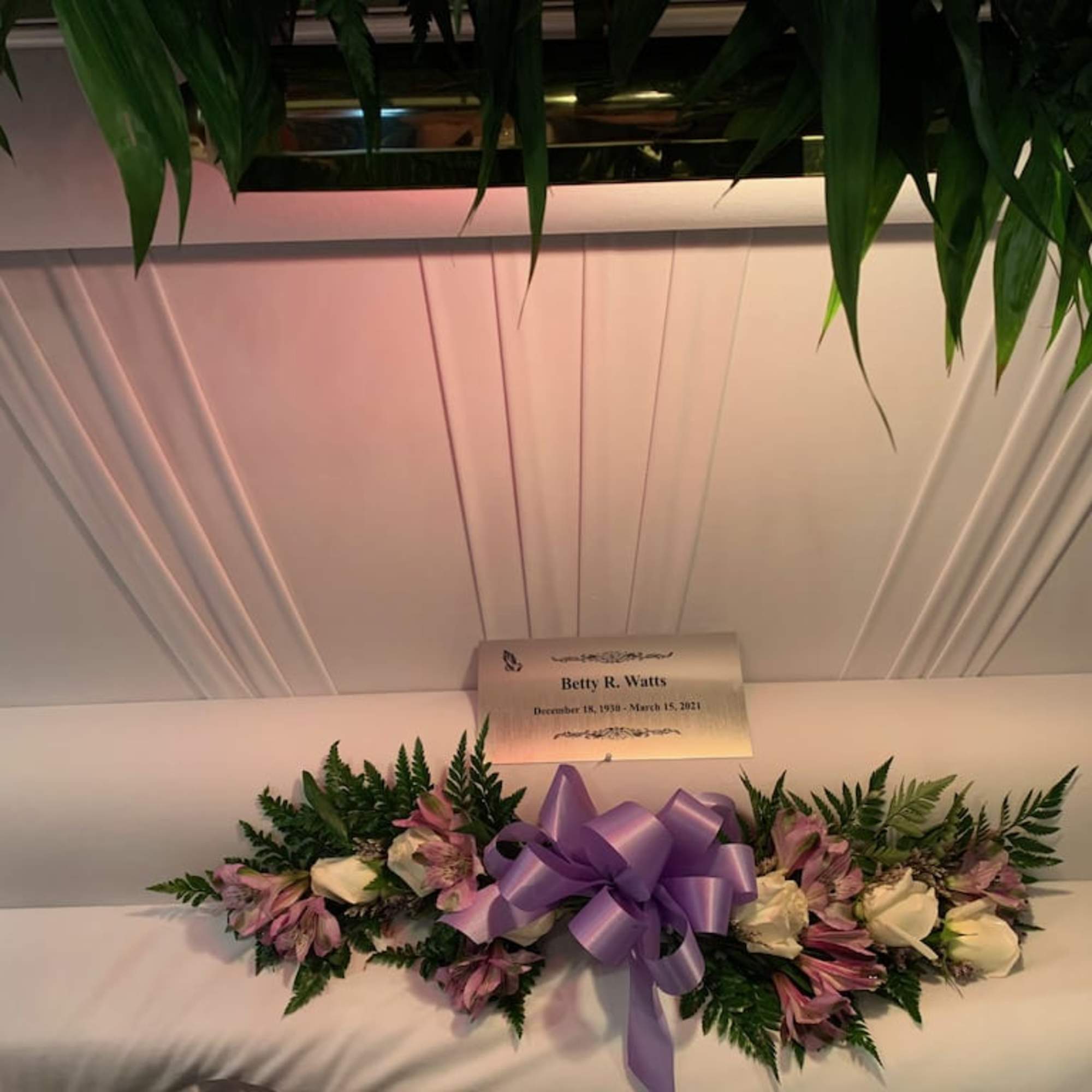 White casket spray with pink flowers and a purple ribbon