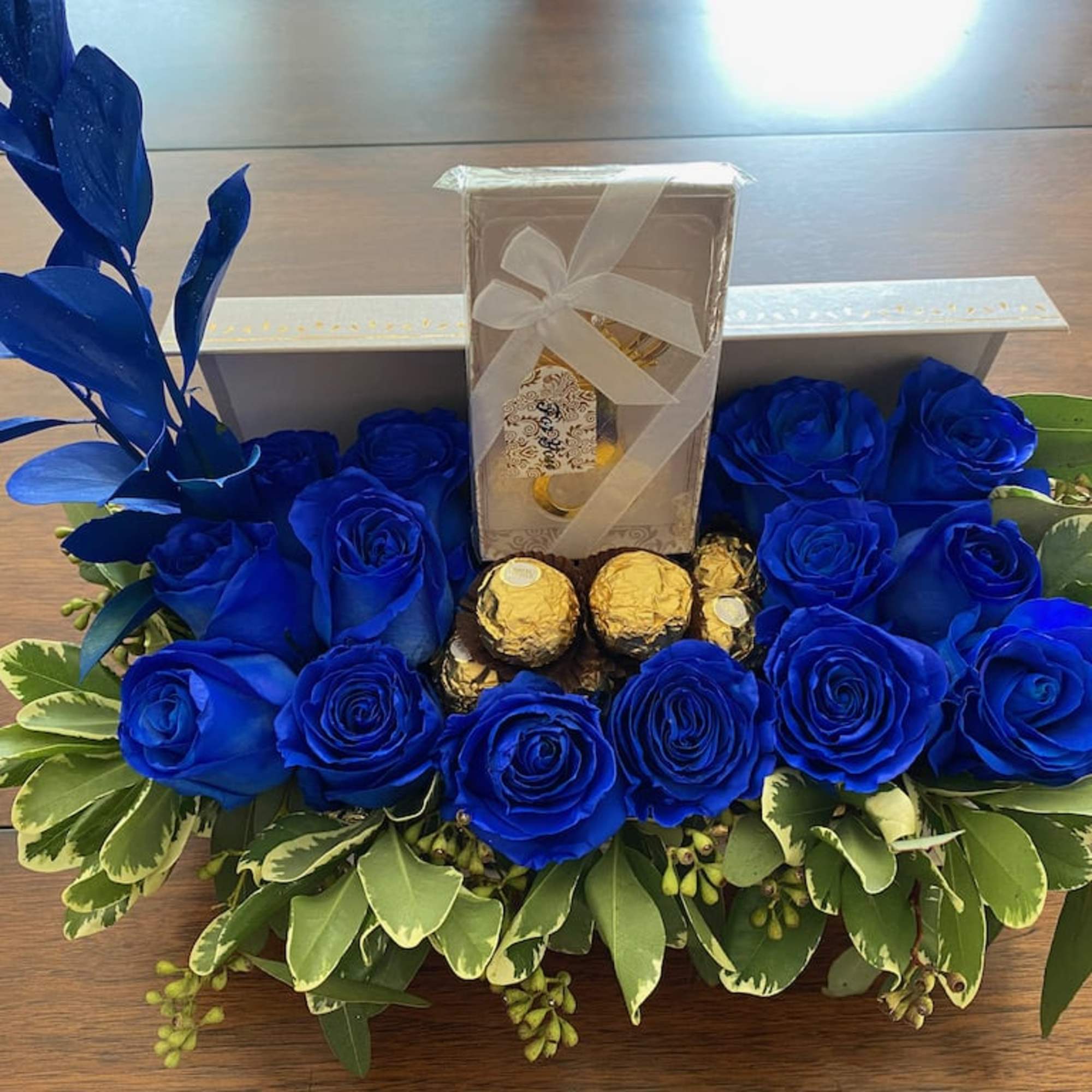 Blue roses arranged around chocolates and a gift box in a low tray
