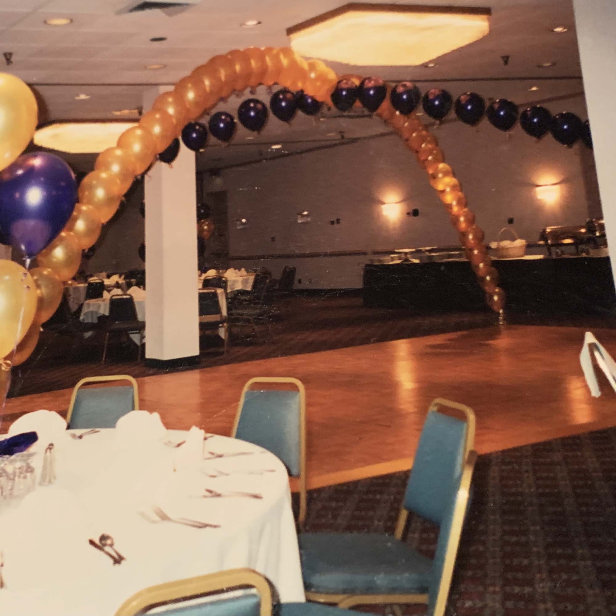 Balloon arches and clusters in gold, purple, and black at a banquet hall