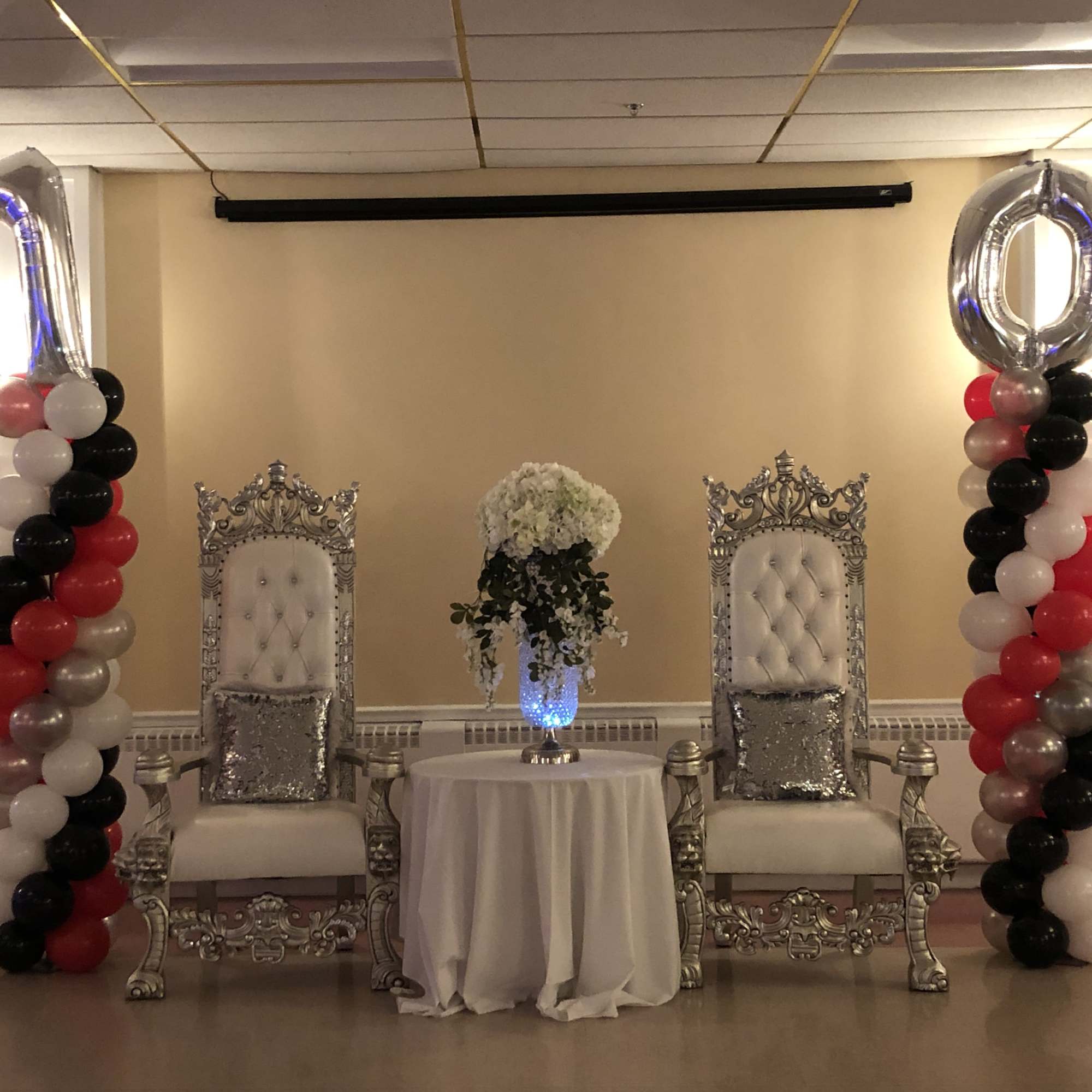 Balloon columns flank two ornate chairs with a floral centerpiece between them.