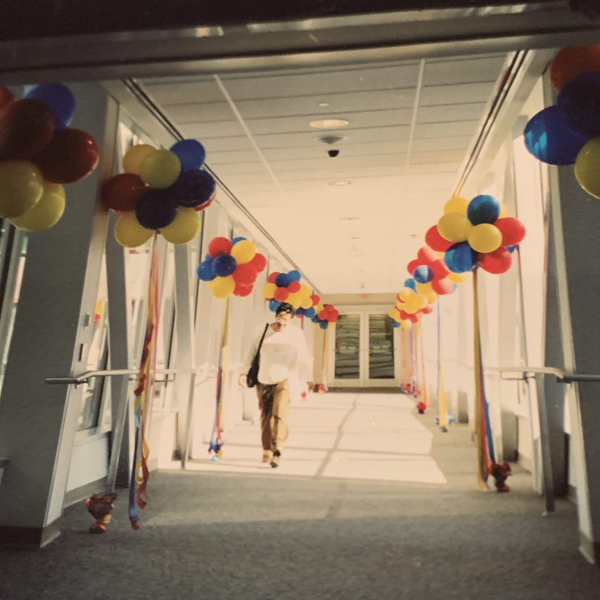 Hallway decorated with clusters of colorful balloons and hanging ribbons.