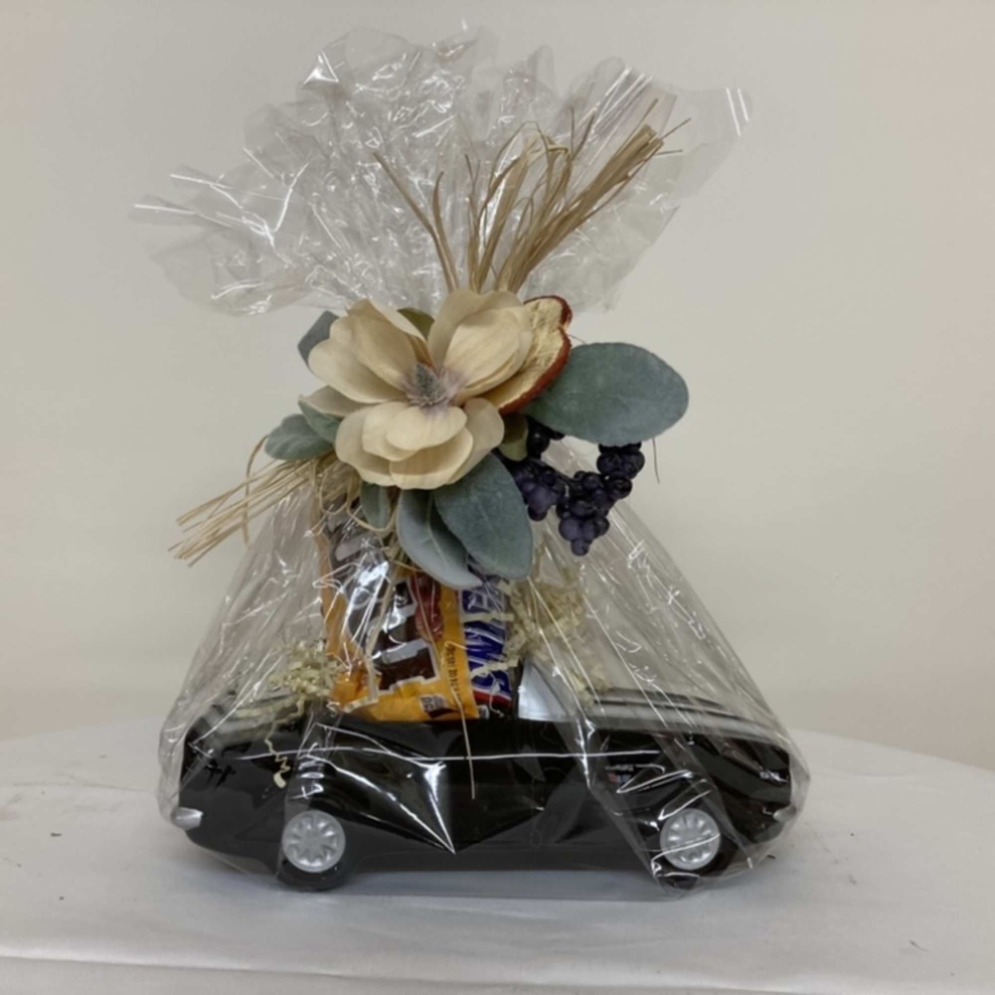 Gift basket wrapped in clear cellophane with flowers and snacks on a black tray