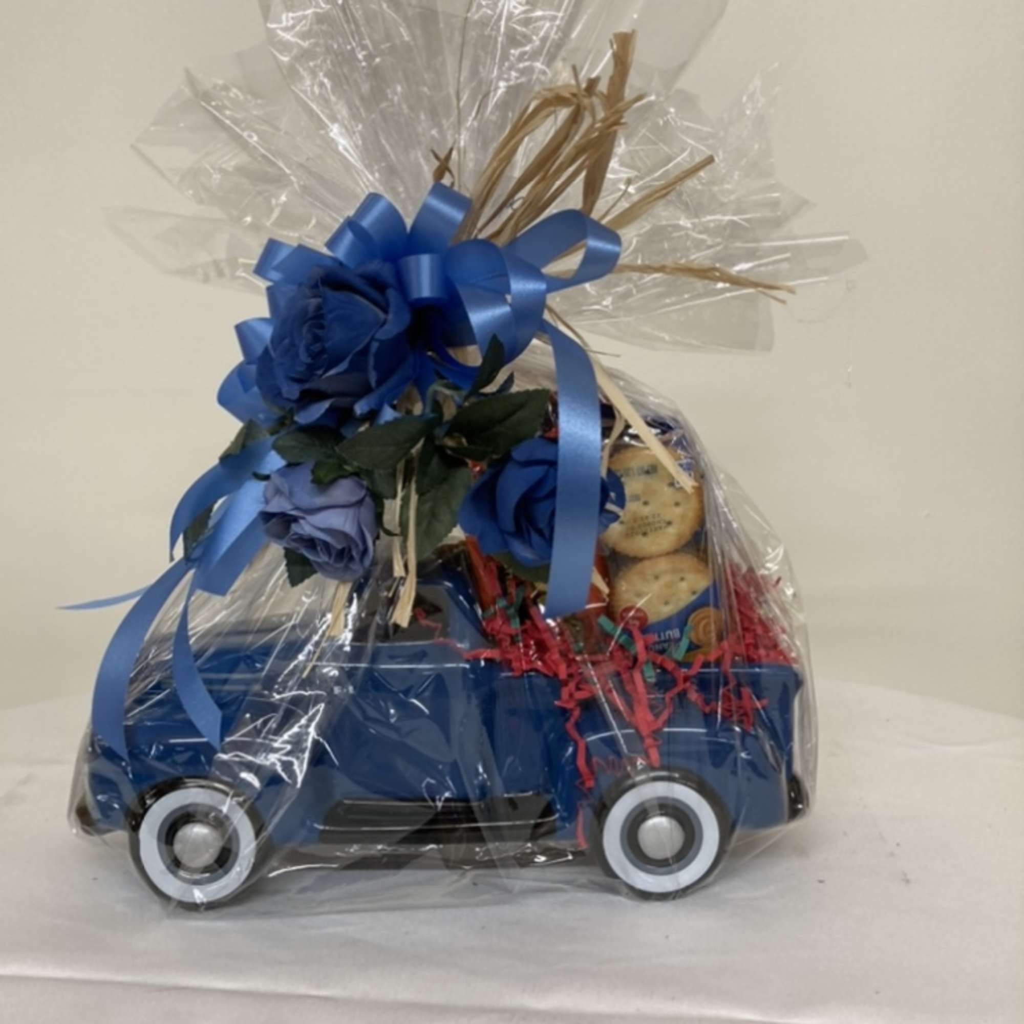 Gift basket wrapped in clear cellophane with blue ribbon and faux flowers on top