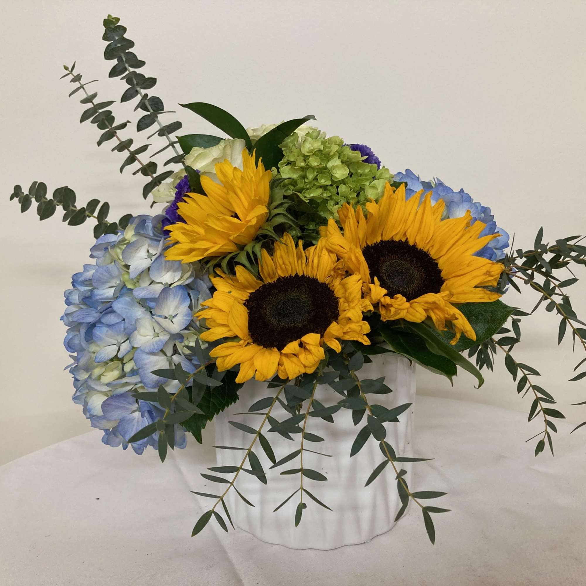 Sunflowers and blue hydrangeas arranged in a white vase