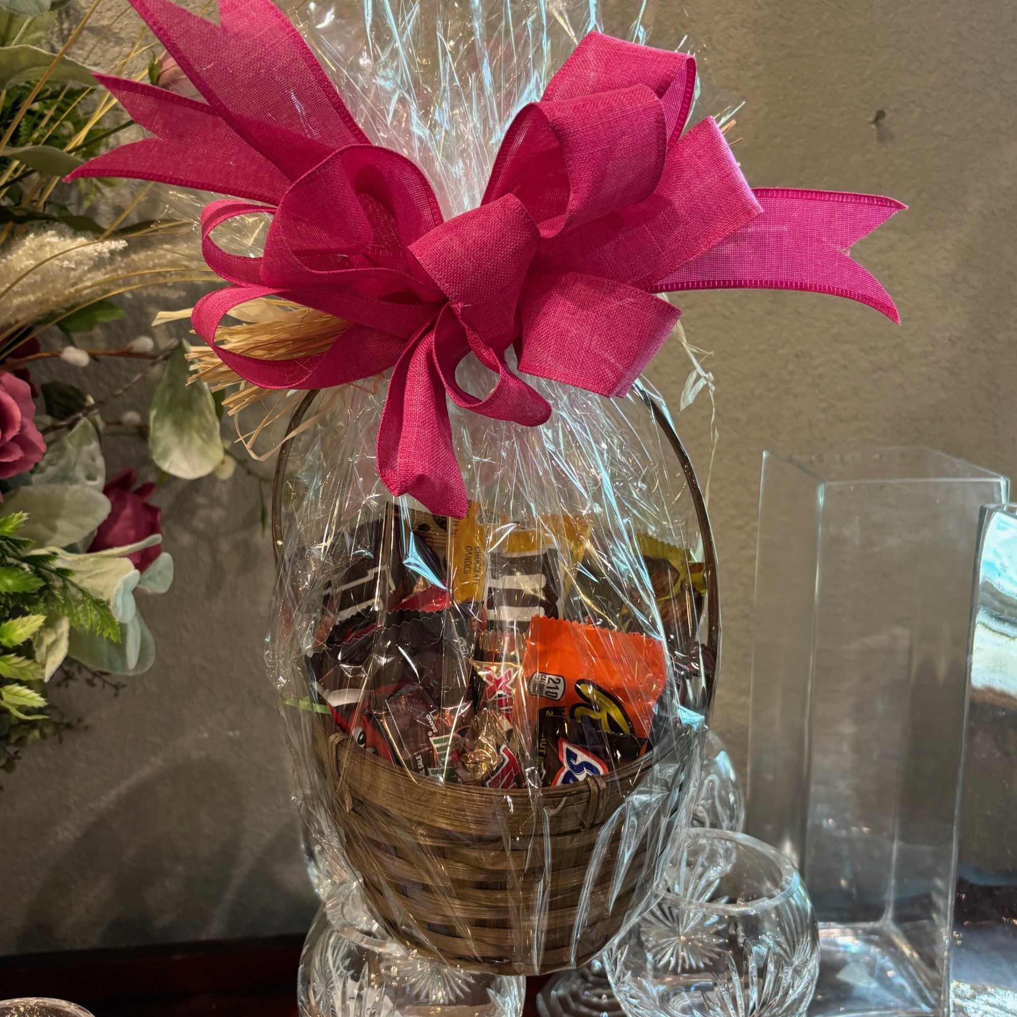 Basket of assorted chocolates wrapped in clear cellophane with a bright pink bow