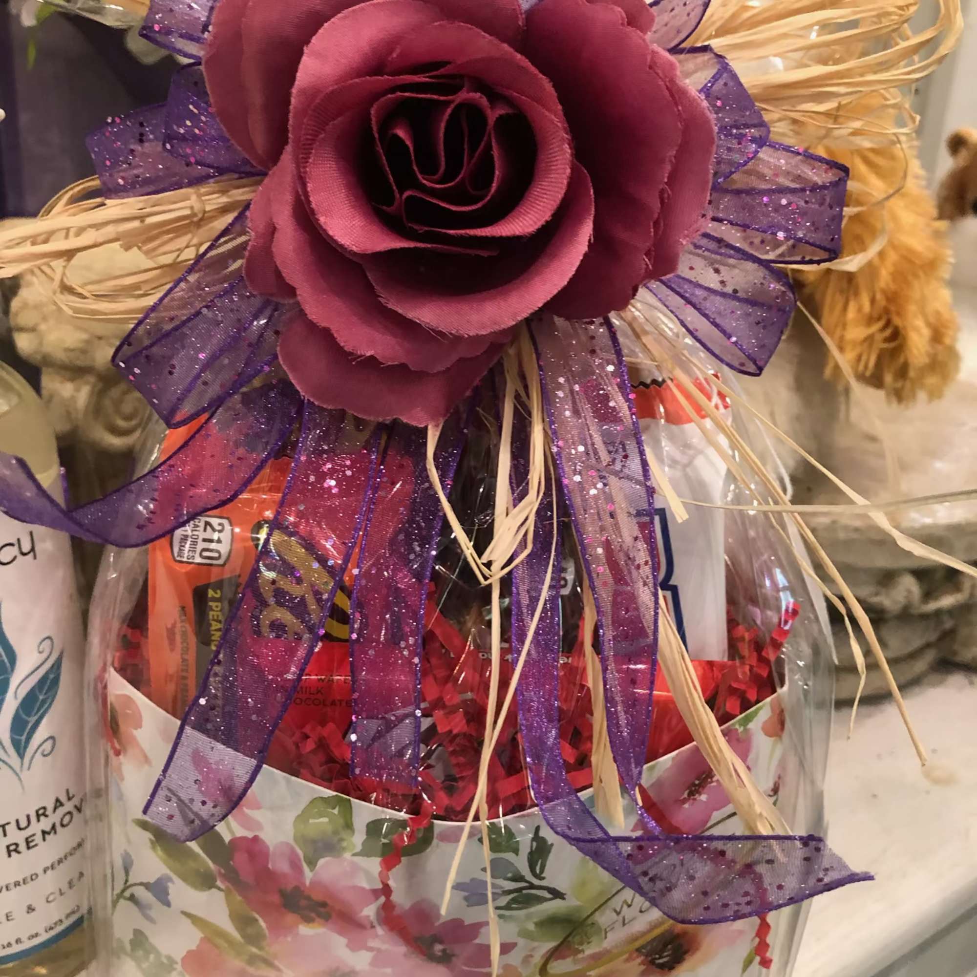 Gift basket topped with a purple fabric rose and ribbon bow