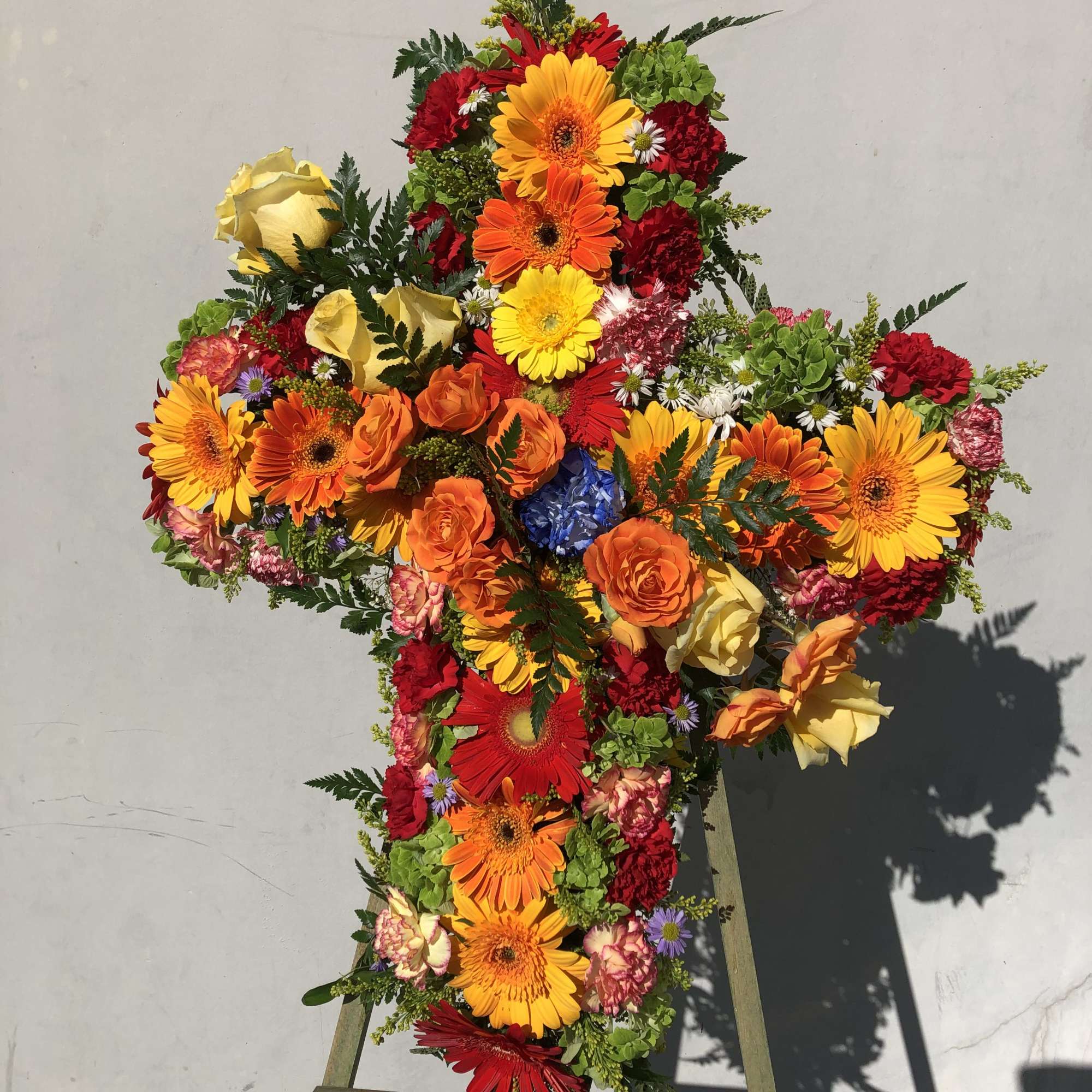 Cross-shaped floral tribute with bright mixed flowers on an easel