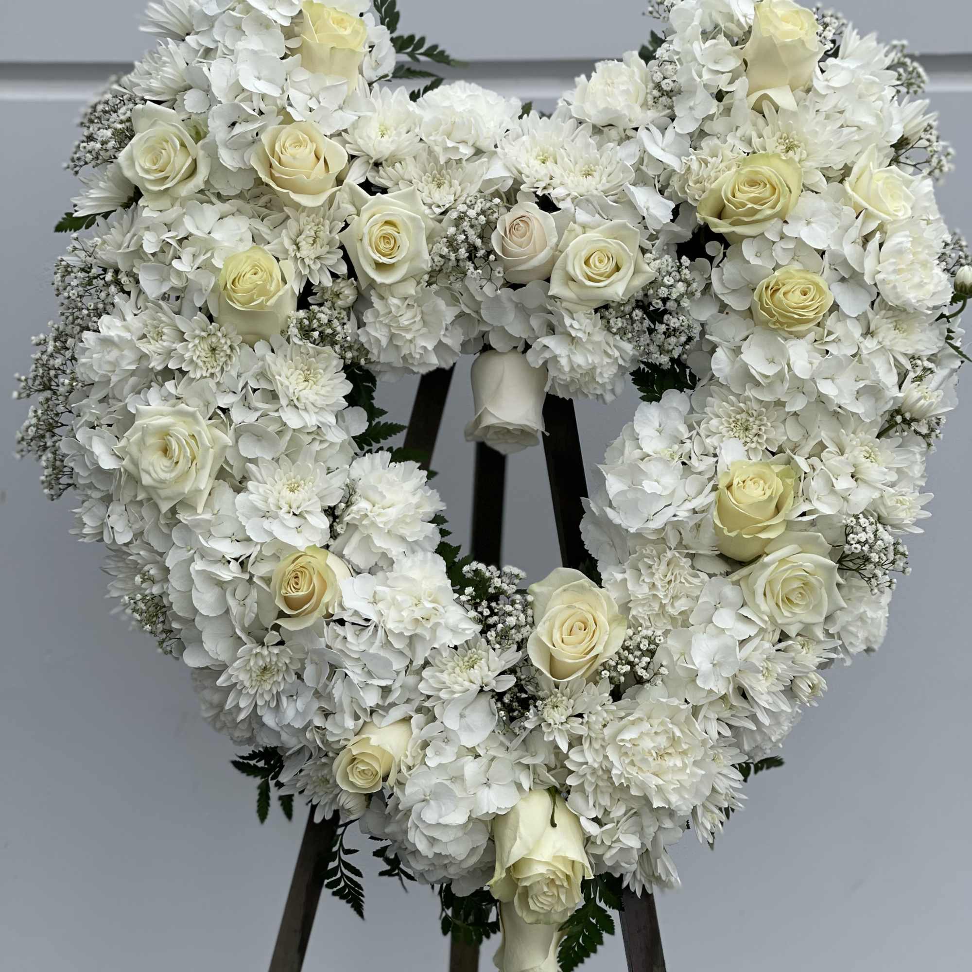 Heart-shaped white floral wreath with cream roses on a stand
