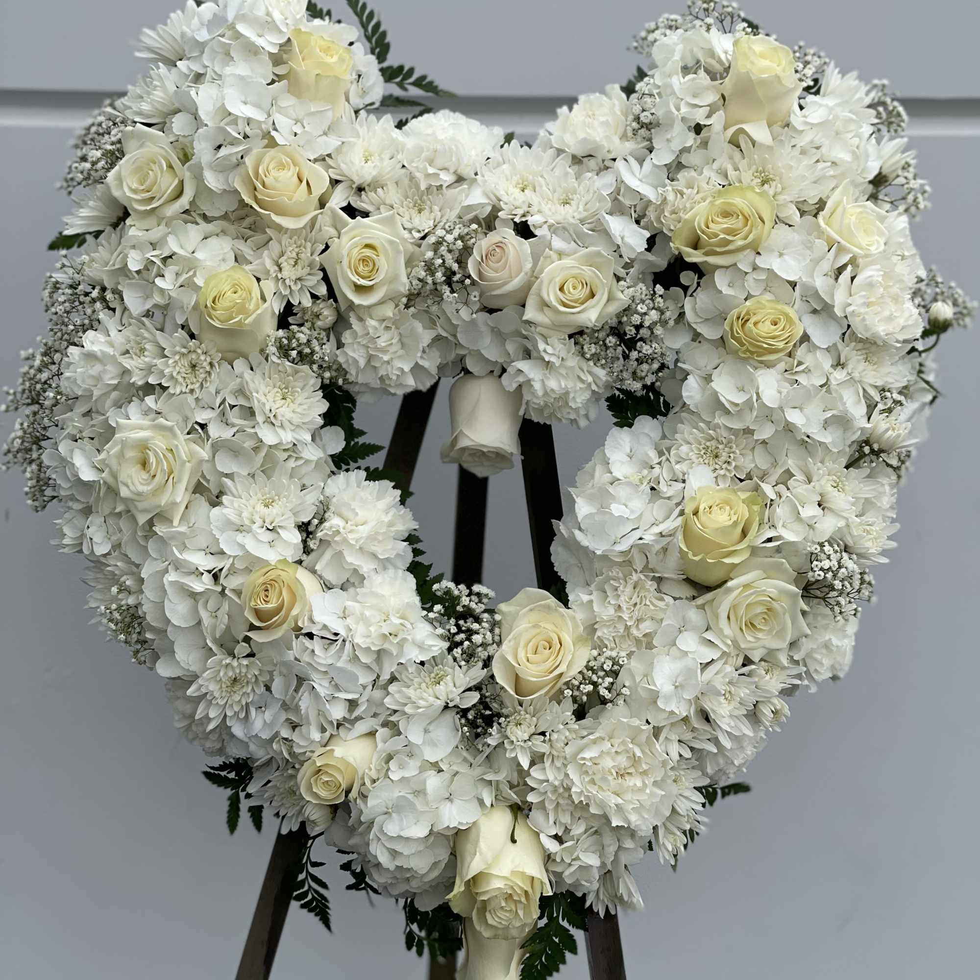 Heart-shaped white floral wreath with cream roses on a stand, photo 2 of 3