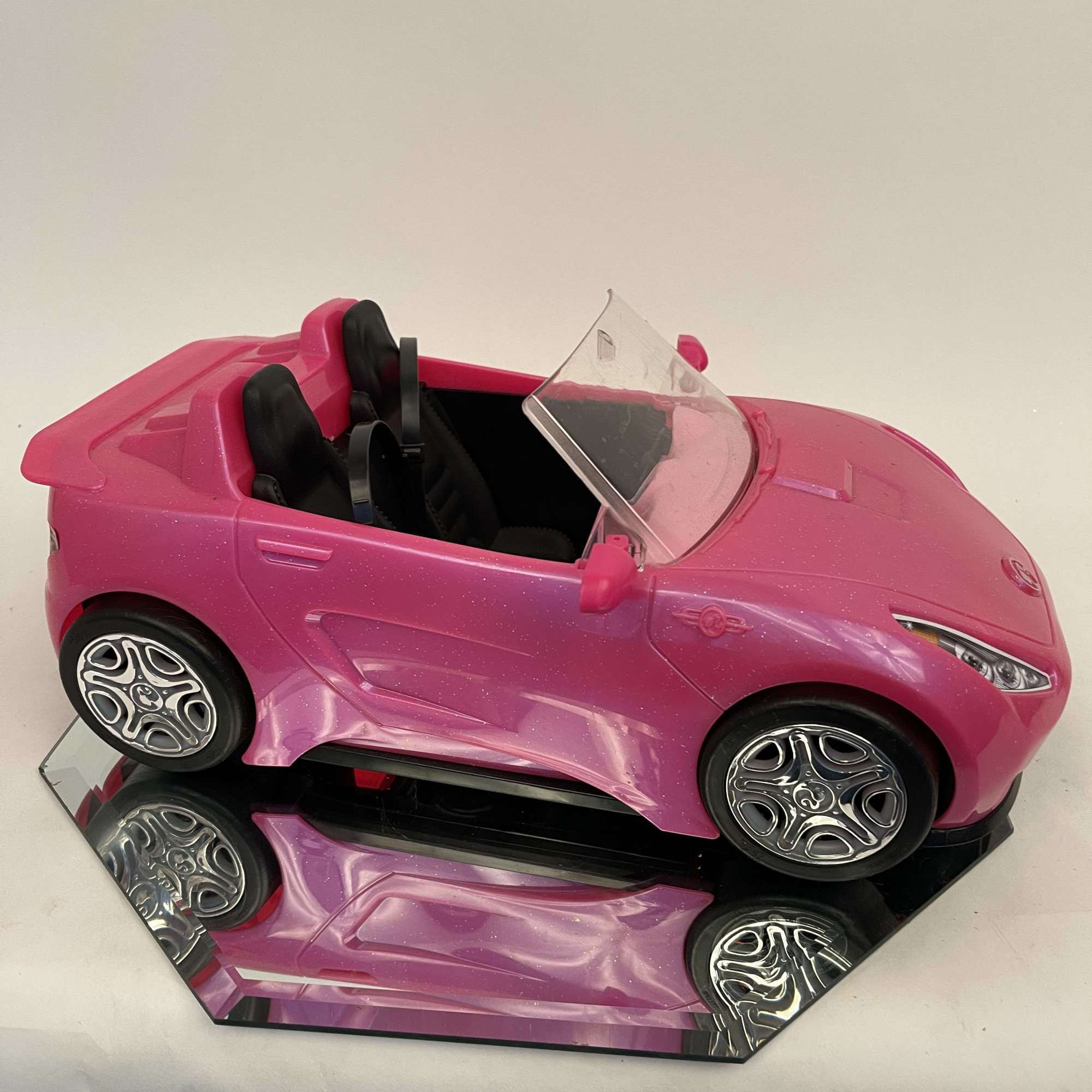 Pink toy convertible car with black seats on a mirrored base