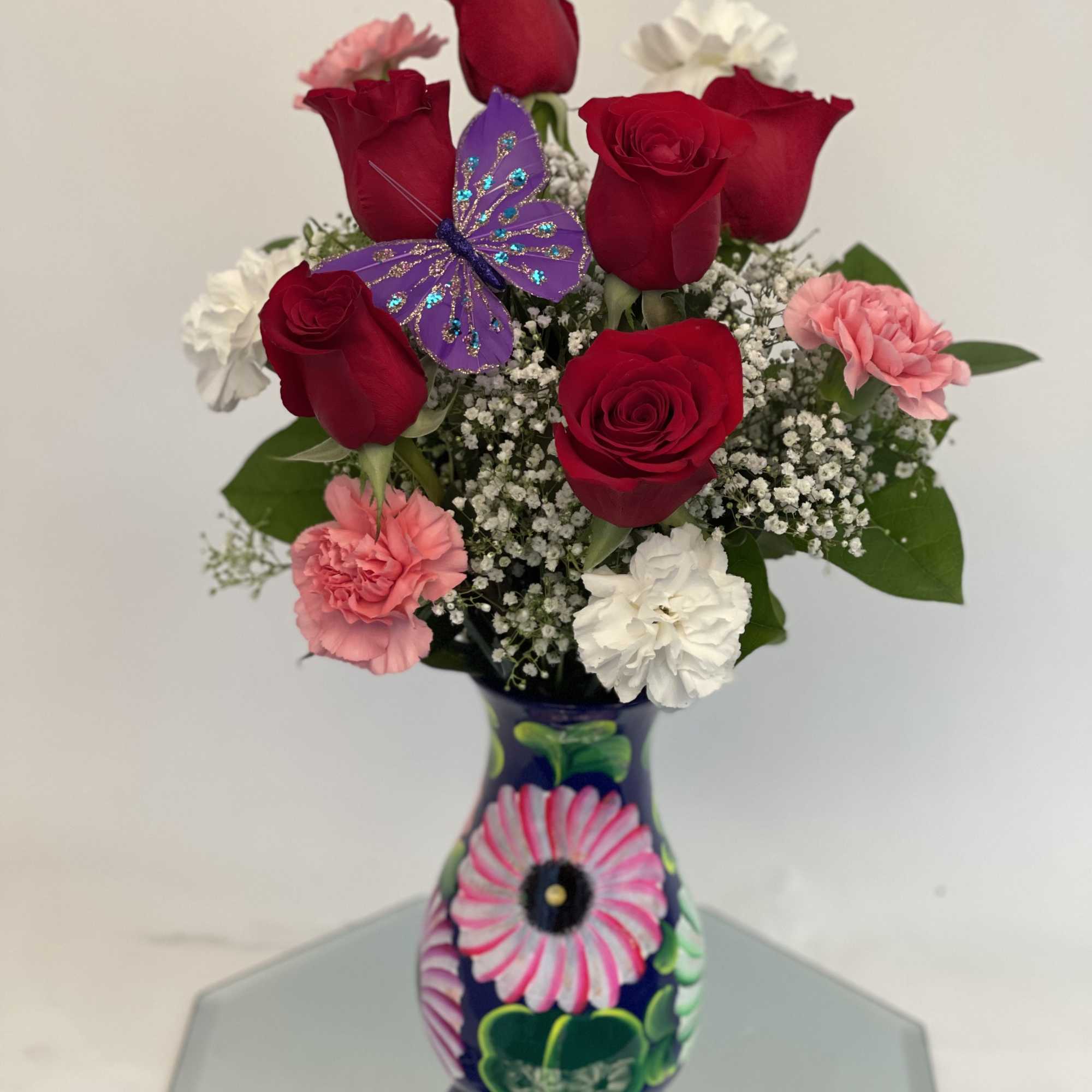 Red roses and pink carnations in a painted vase with a purple butterfly decoration