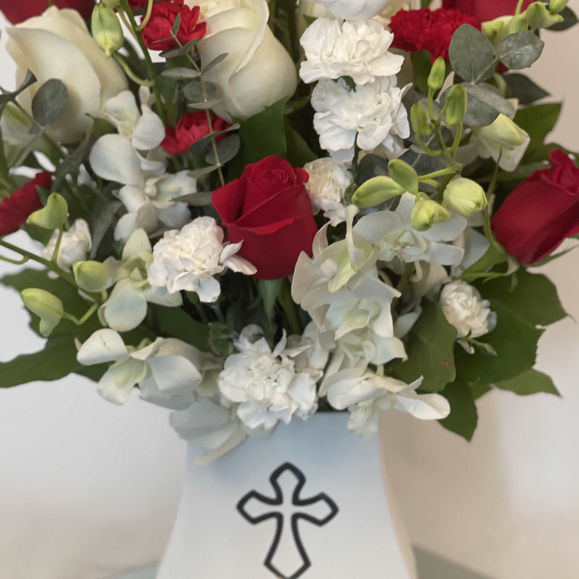 Red and white roses with white orchids in a white vase with a cross emblem.