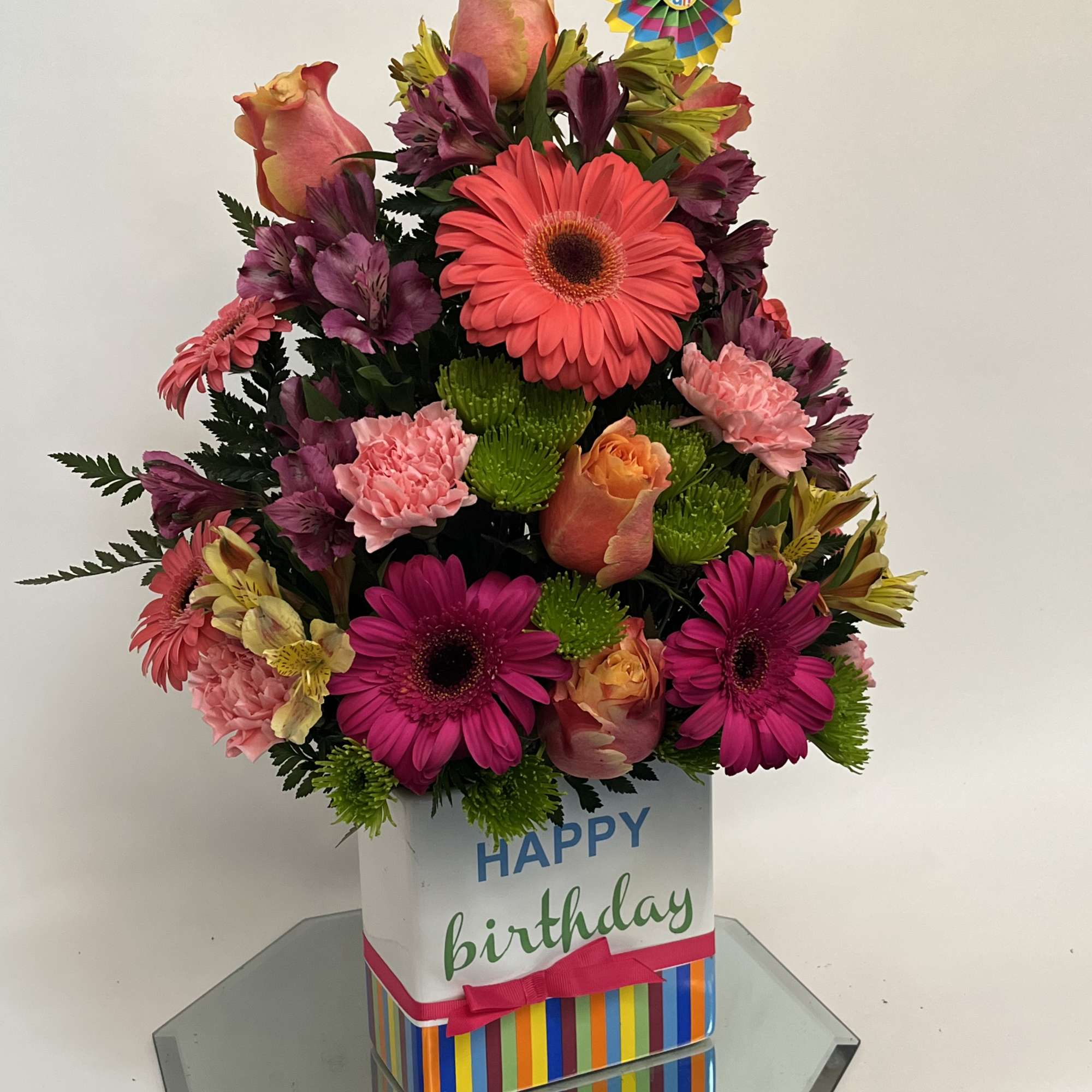 Birthday flower arrangement in a striped gift box with a rosette topper