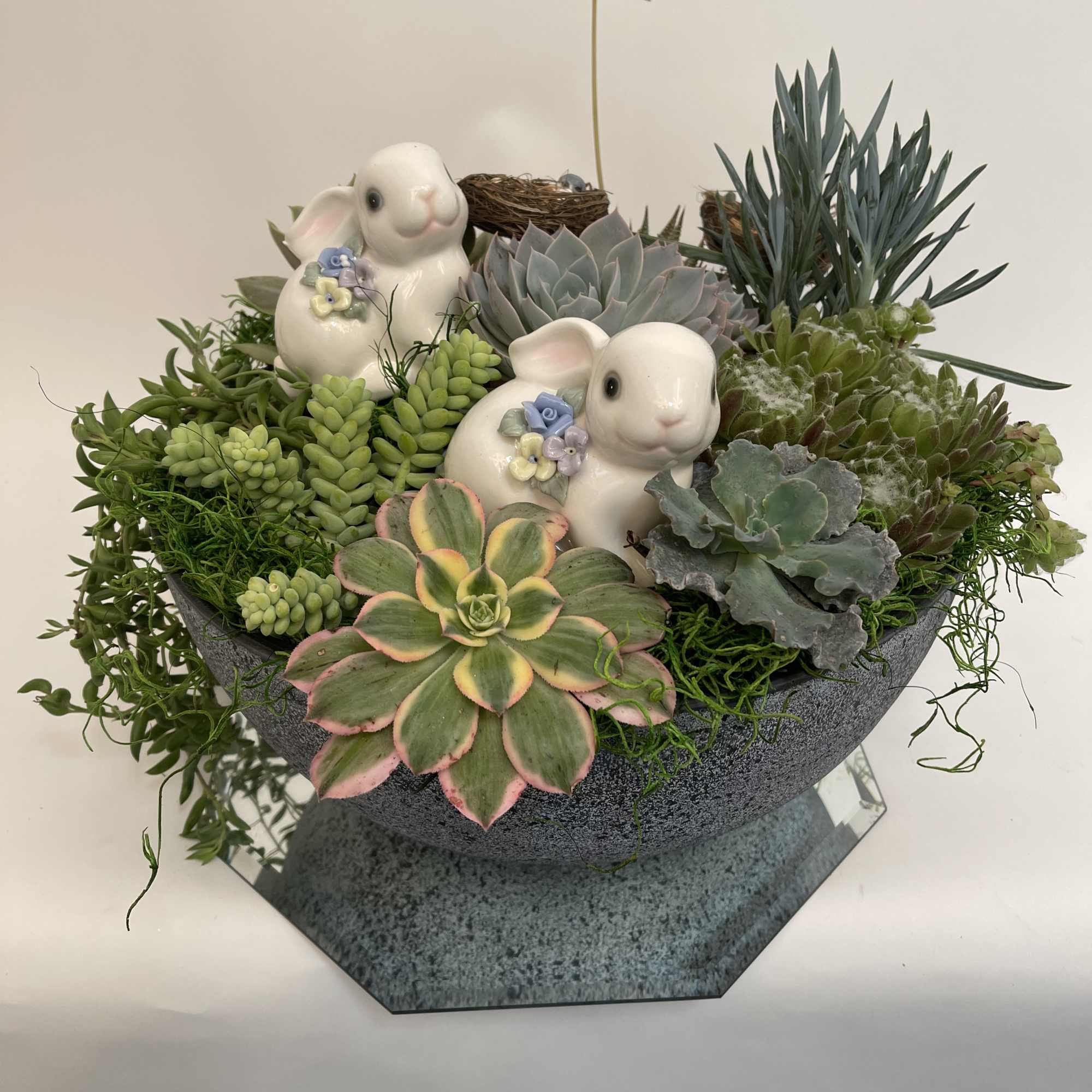 Succulent arrangement with two ceramic bunny figurines in a gray bowl