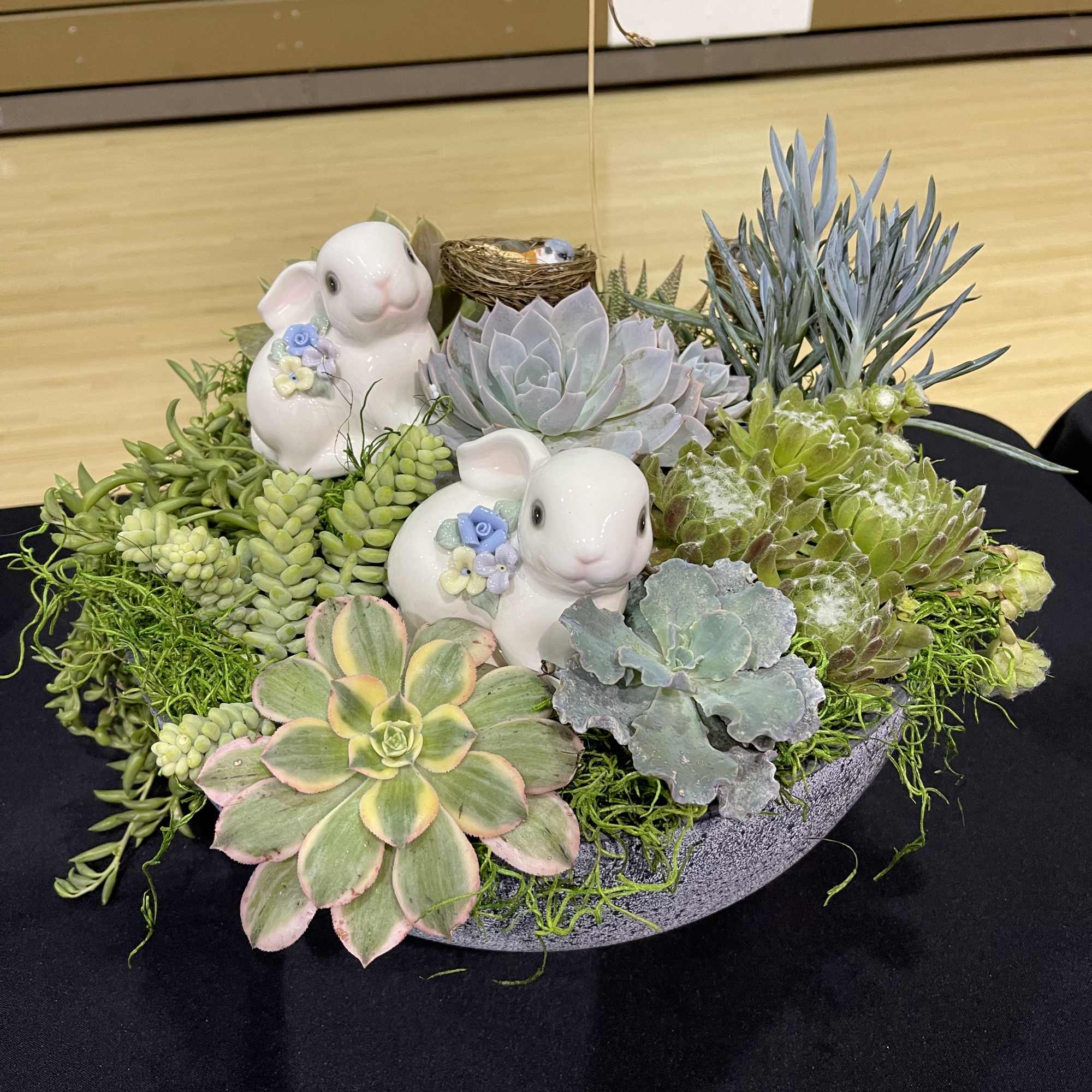 Succulent arrangement in a shallow bowl with two ceramic rabbits