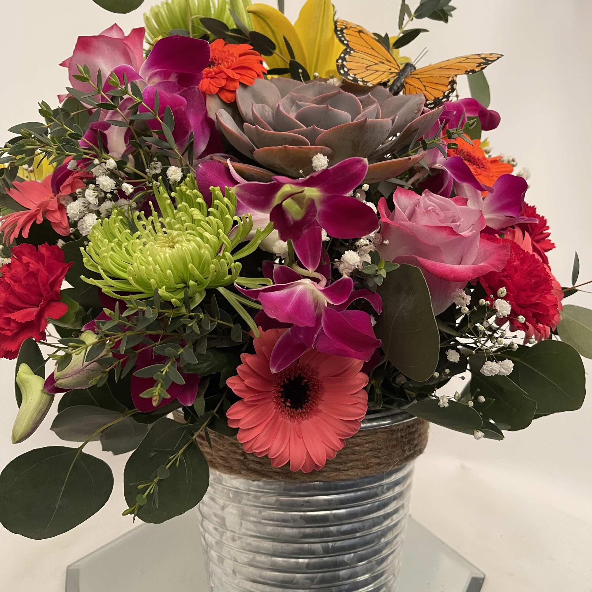 Colorful bouquet in a metal vase with roses, orchids, and a butterfly accent