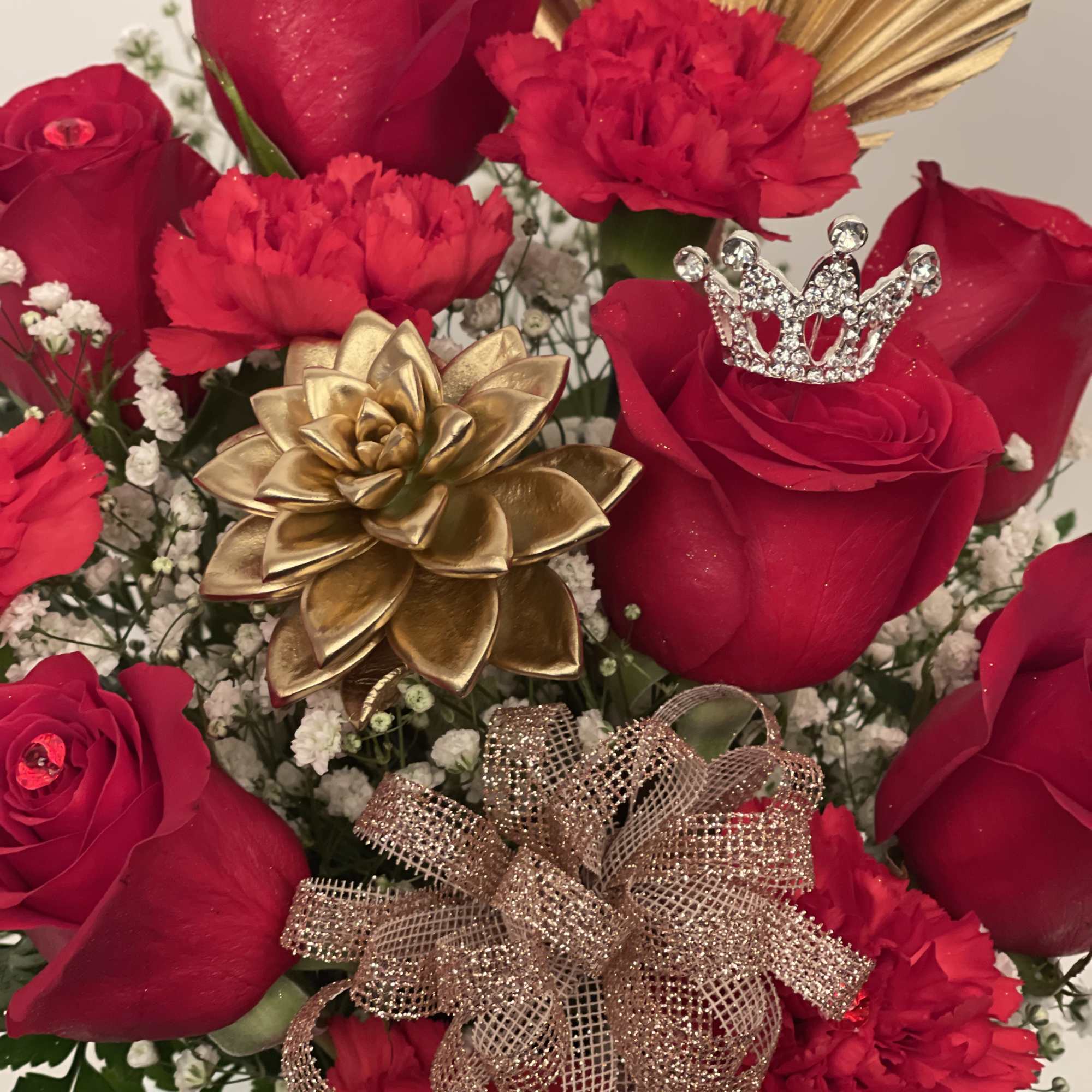 Red roses and carnations with gold accents and a glittery bow