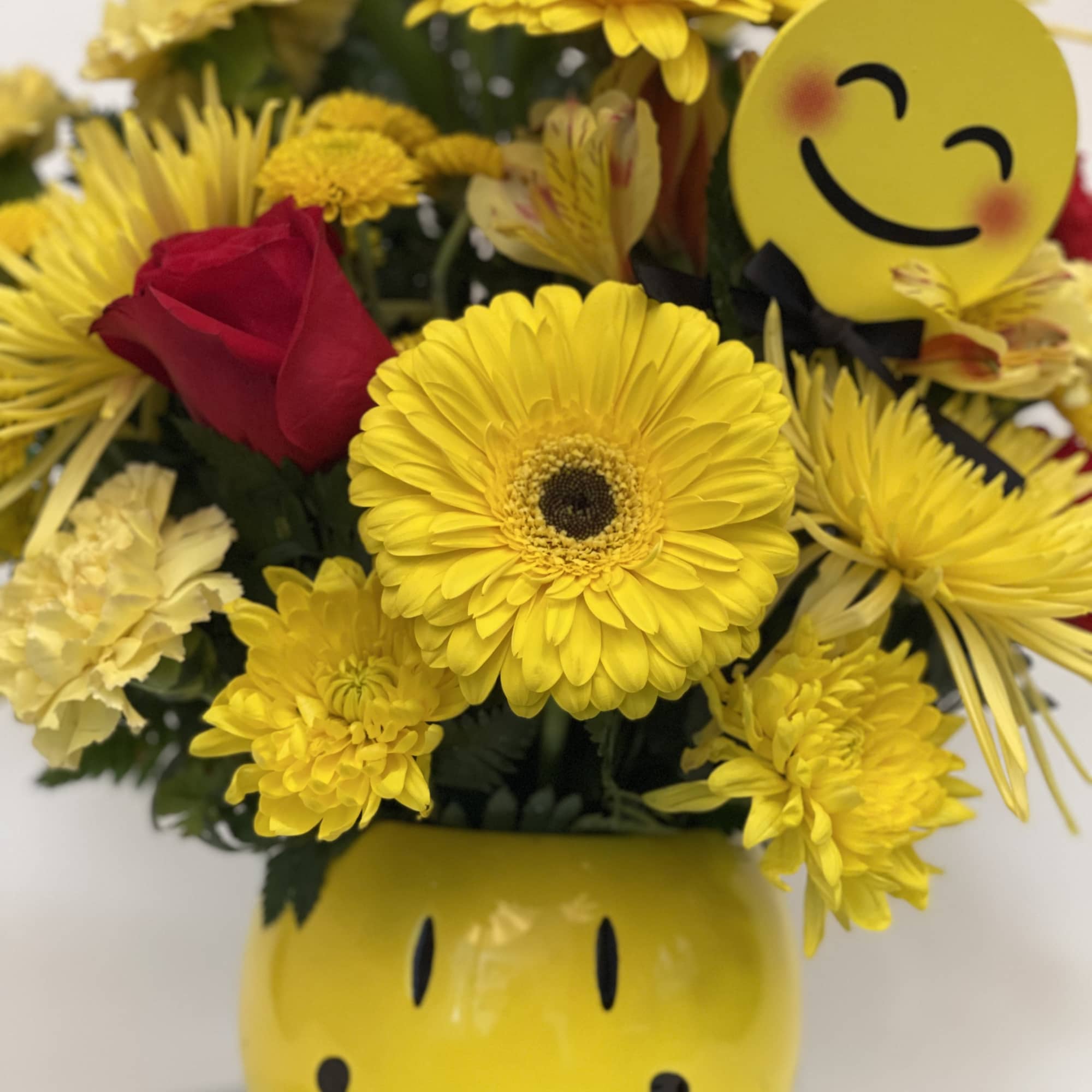 Yellow and red flower bouquet in a smiley-face vase with a smiley pick